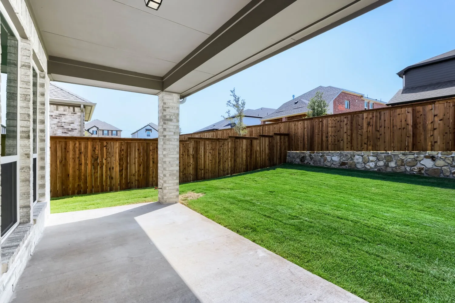 Covered outdoor patio with a concrete slab, stone column, and a flush-mount ceiling light