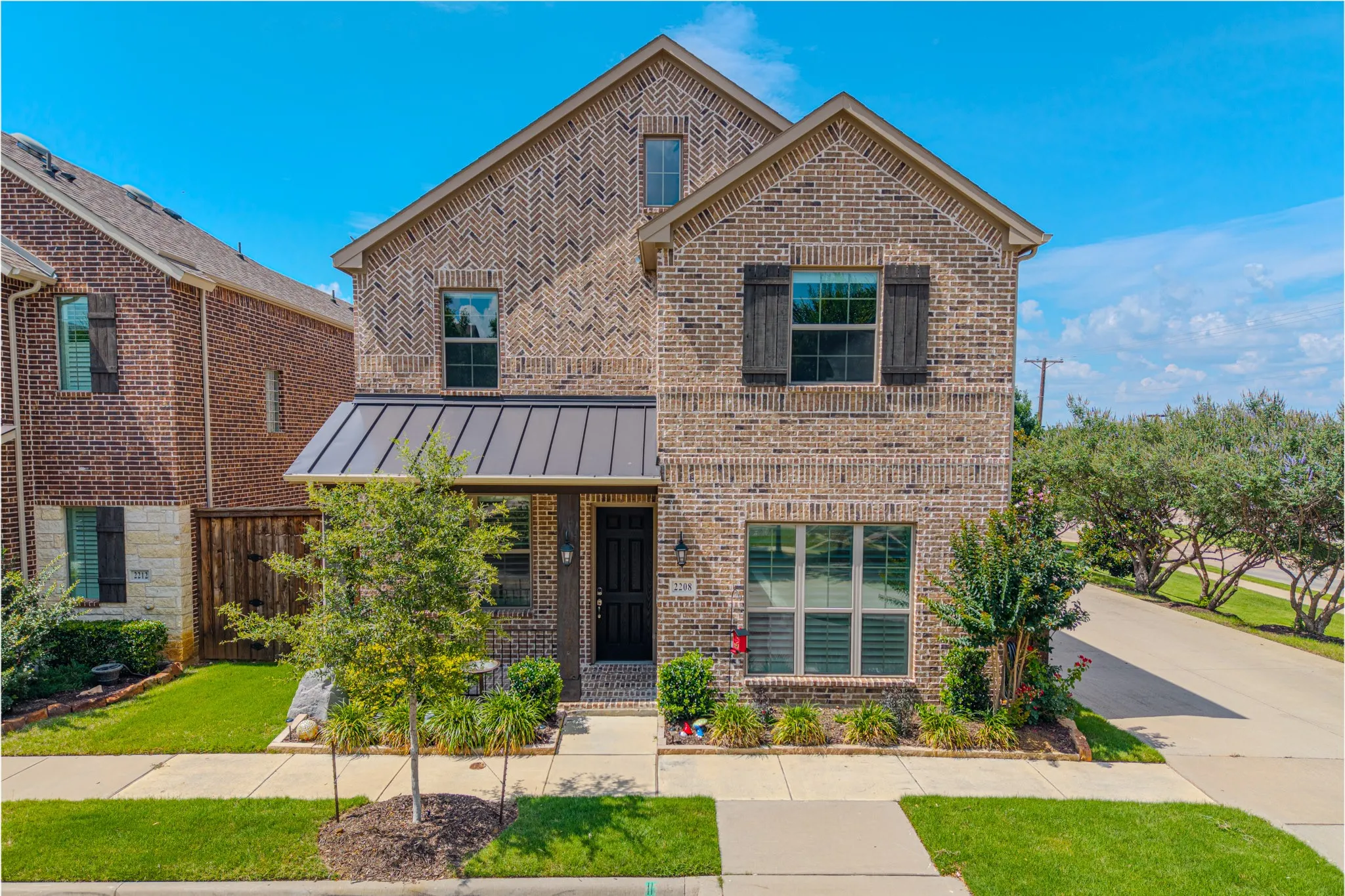 Two-story brick exterior featuring a metal awning over the entrance, decorative shutters, and established landscaping