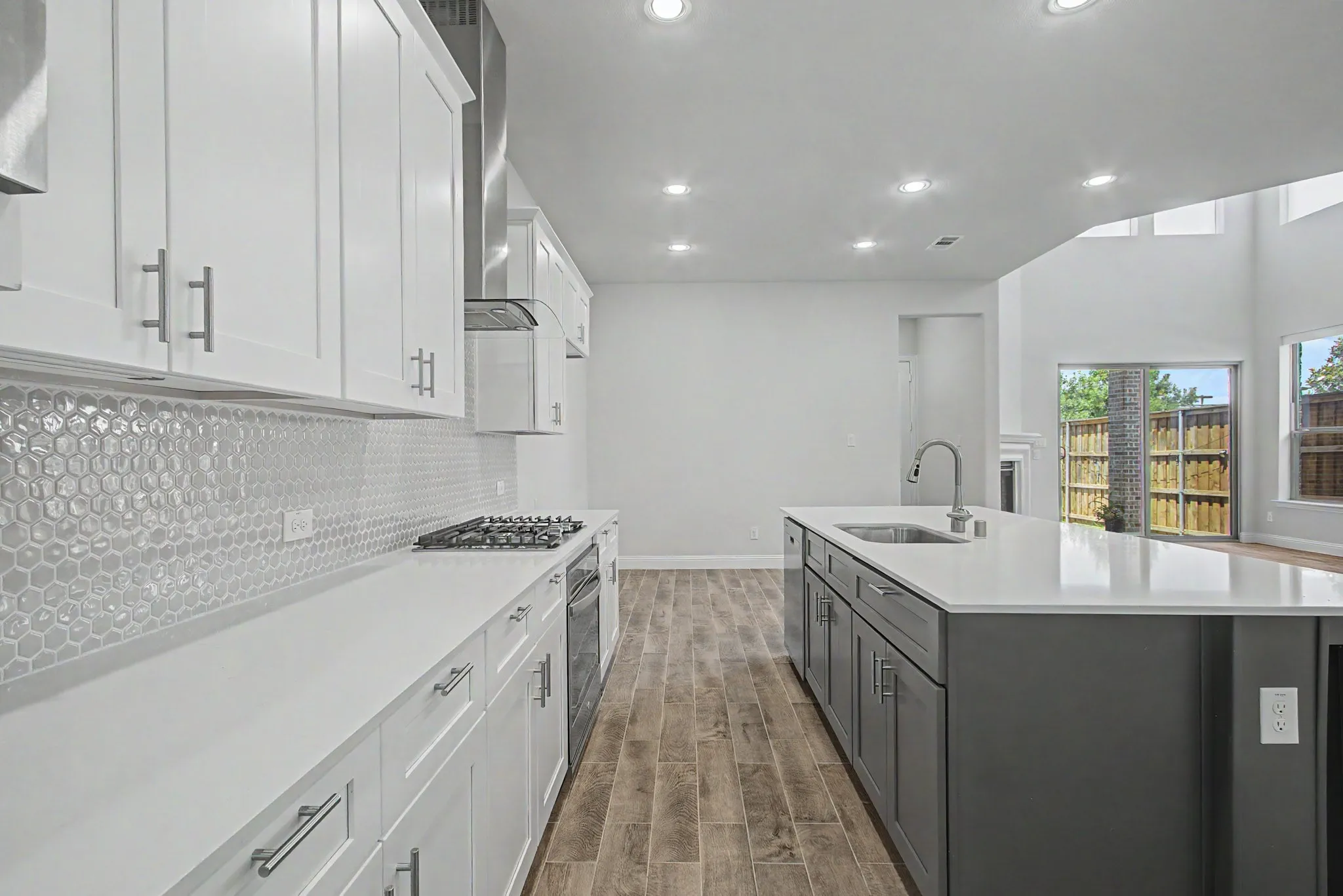 Modern kitchen featuring an extended island with integrated sink, white shaker-style cabinetry, and a textured hexagonal tile backsplash