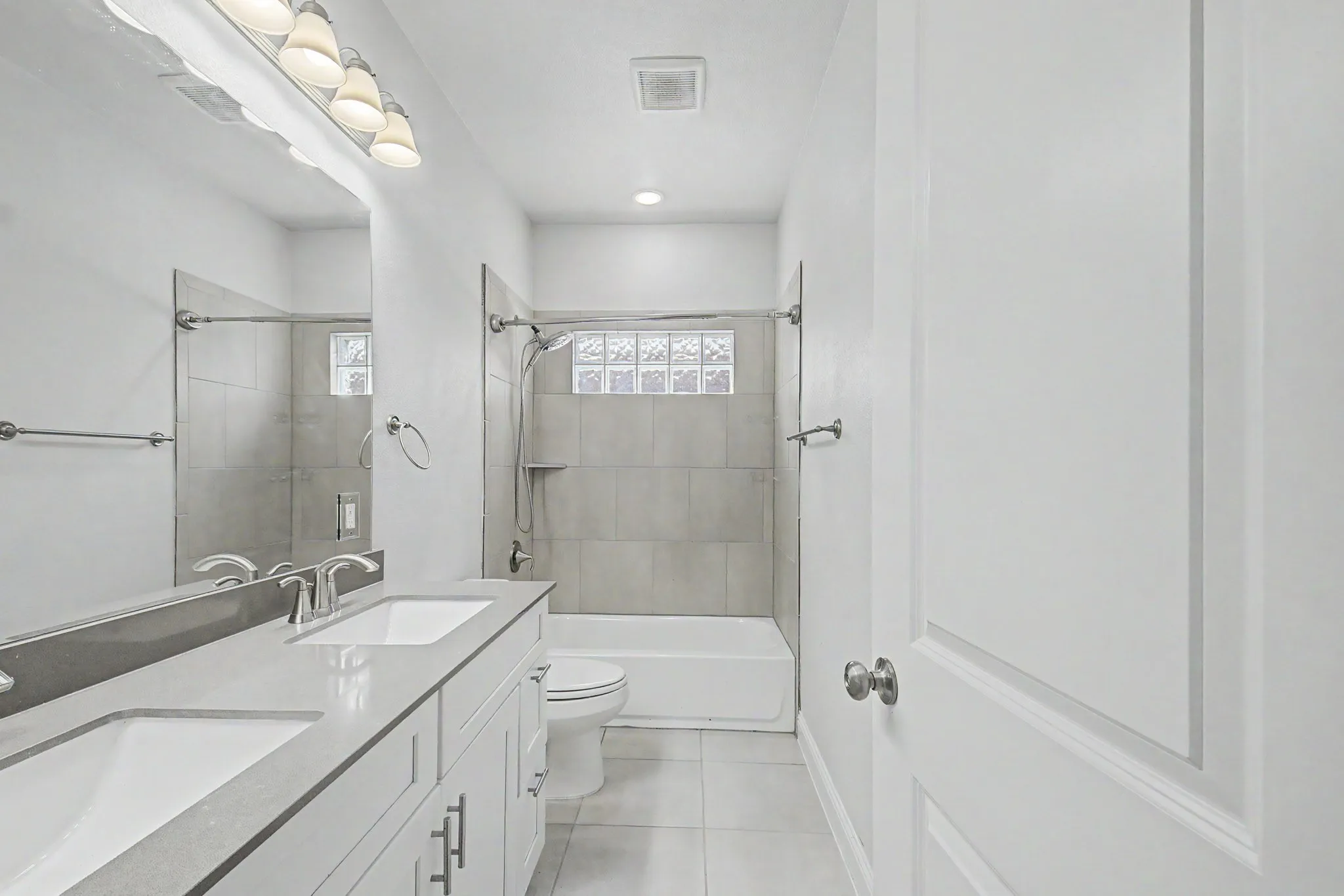Contemporary bathroom featuring a dual vanity with undermount sinks, a bathtub with a tiled shower surround, glass block window accents, and recessed lighting