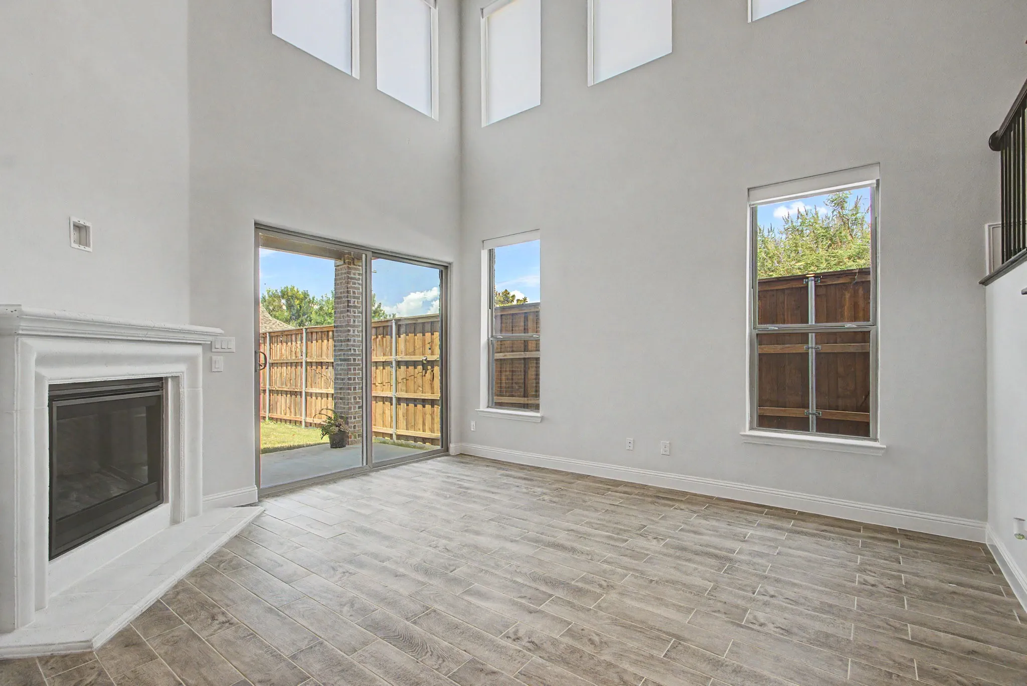 Spacious room featuring wood-finish flooring, a contemporary fireplace with a classic mantel, and multiple large windows