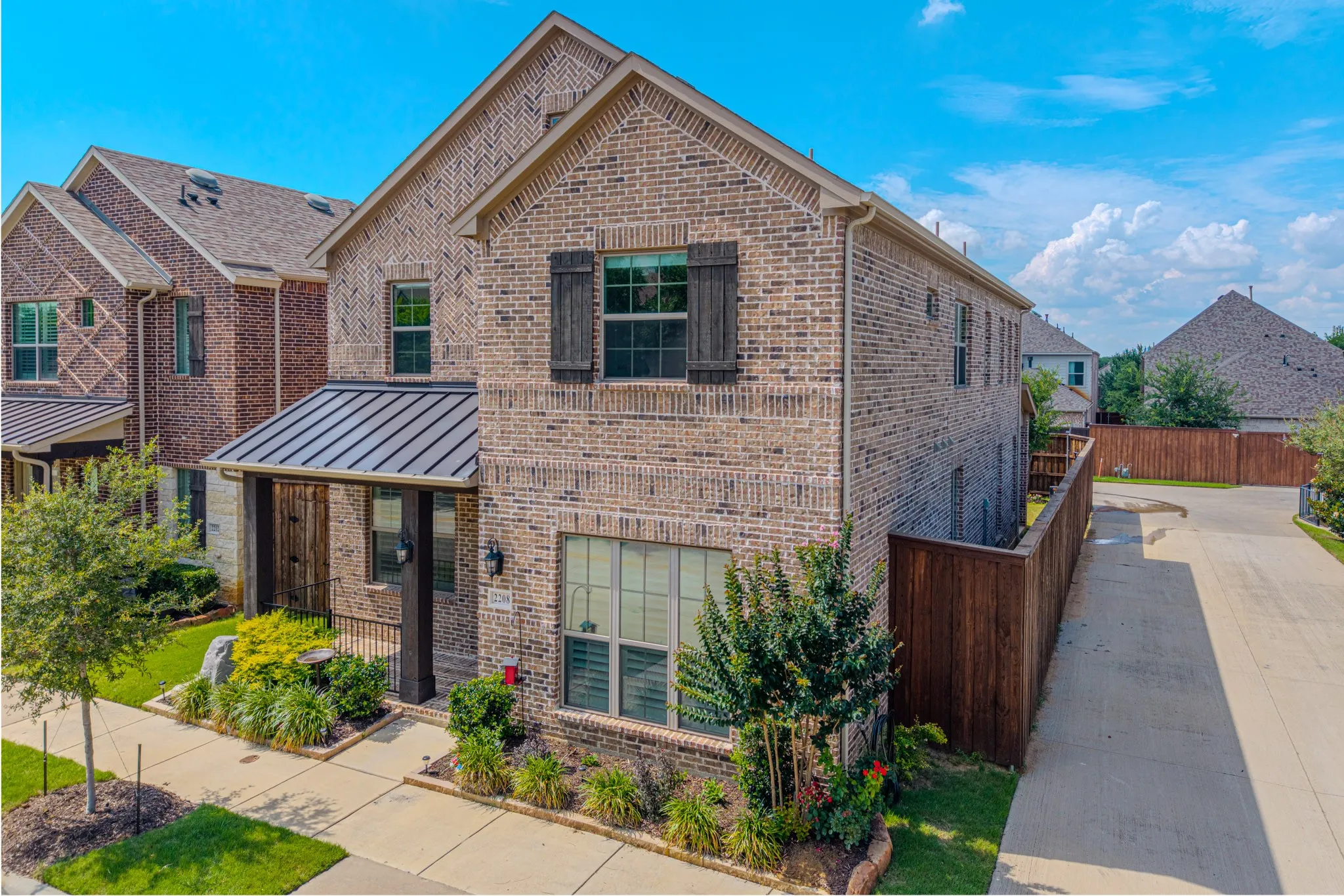 Brick facade with decorative shutters, covered entry with metal awning, and landscaped front yard