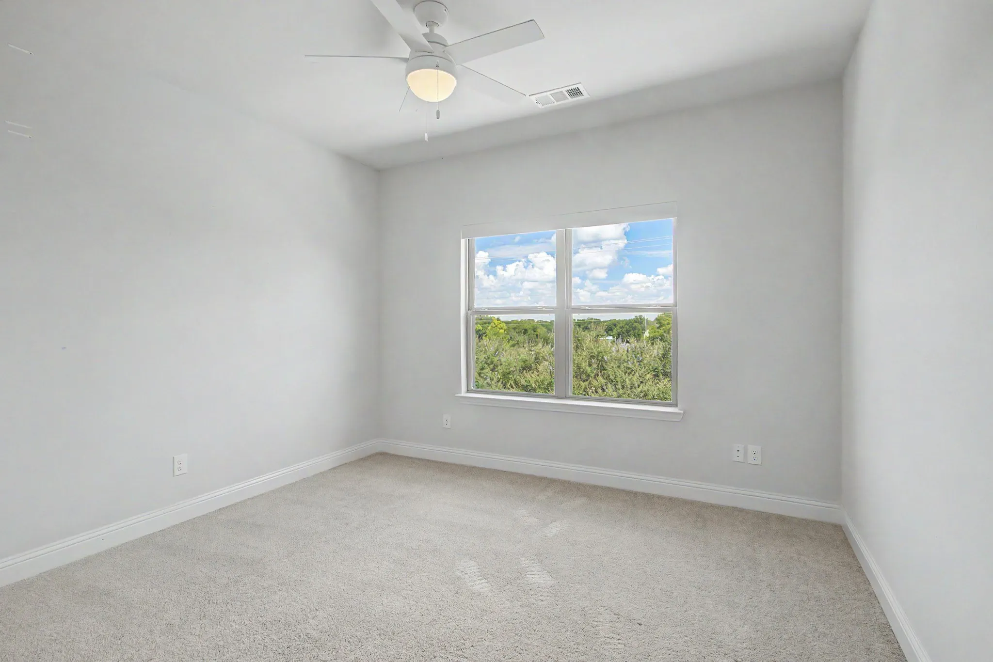 Bright room featuring a large window, plush carpet, white baseboards, and a ceiling fan with integrated lighting
