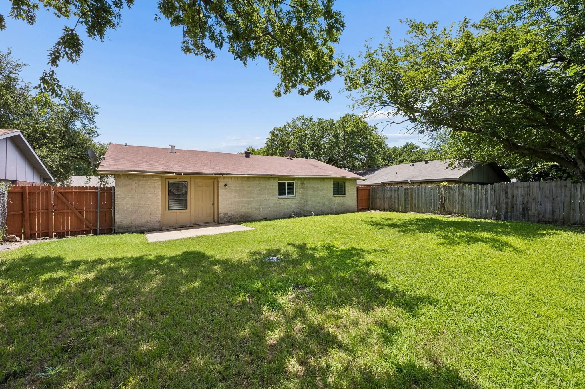 Spacious backyard with a large grass lawn, mature perimeter trees, and wood fencing