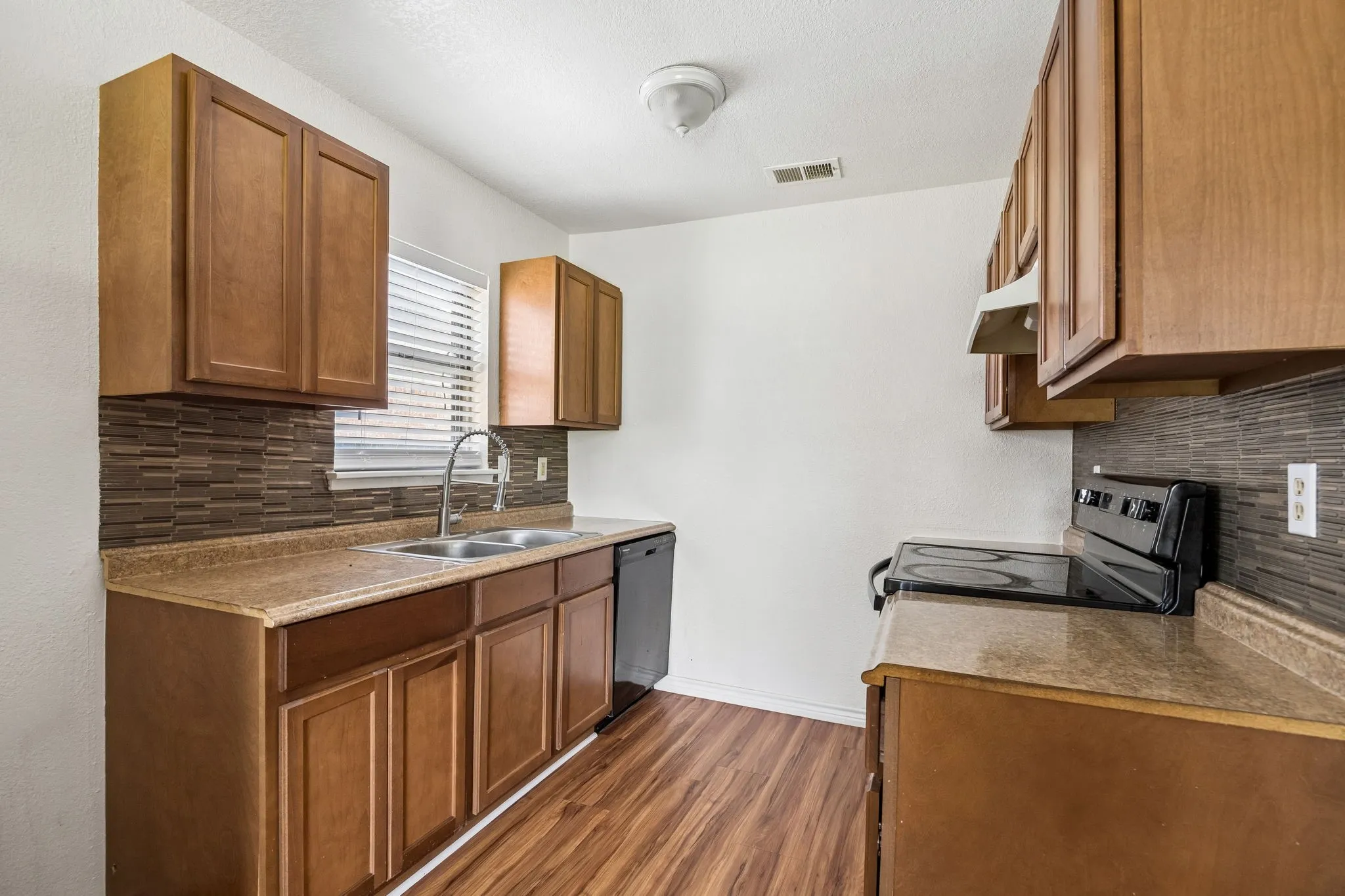 Kitchen featuring wood-finish cabinetry, a stainless steel double basin sink with a high arc faucet, and a black electric range
