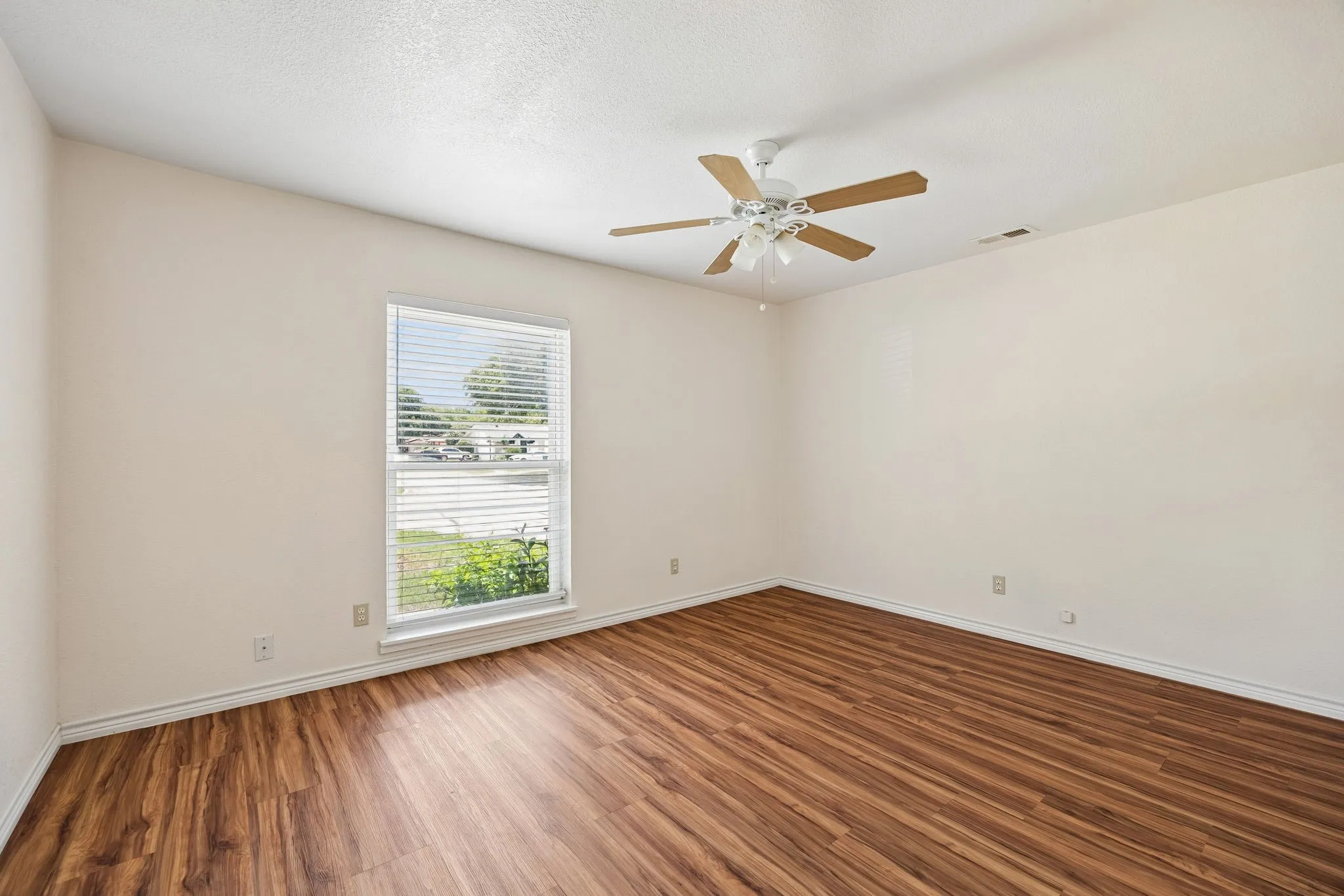 Spacious room featuring wood-finish flooring, a ceiling fan with light fixture, and a window with horizontal blinds