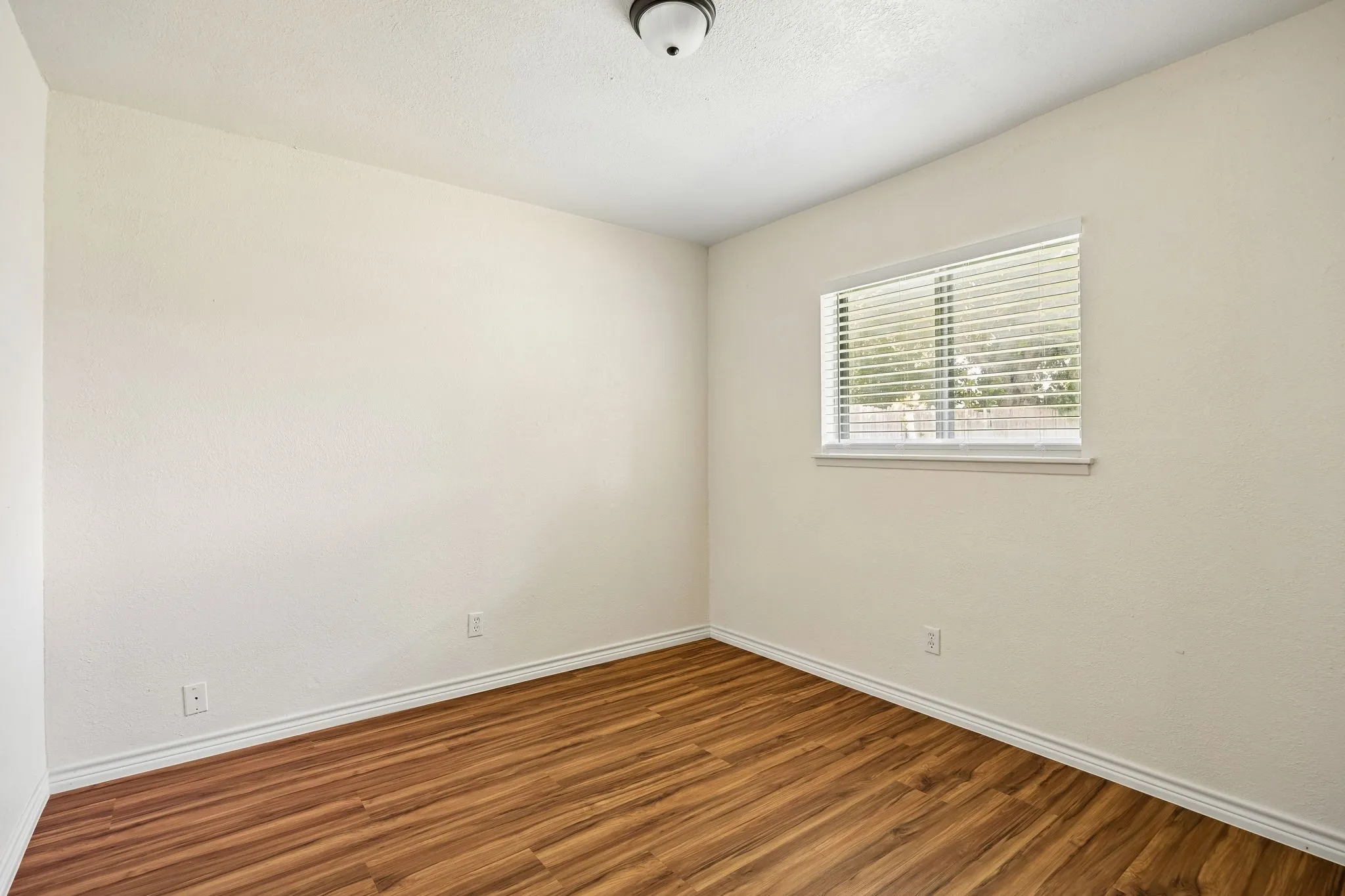 Room featuring wood-finish flooring, neutral wall tones, window with horizontal blinds, and a flush-mount ceiling light fixture