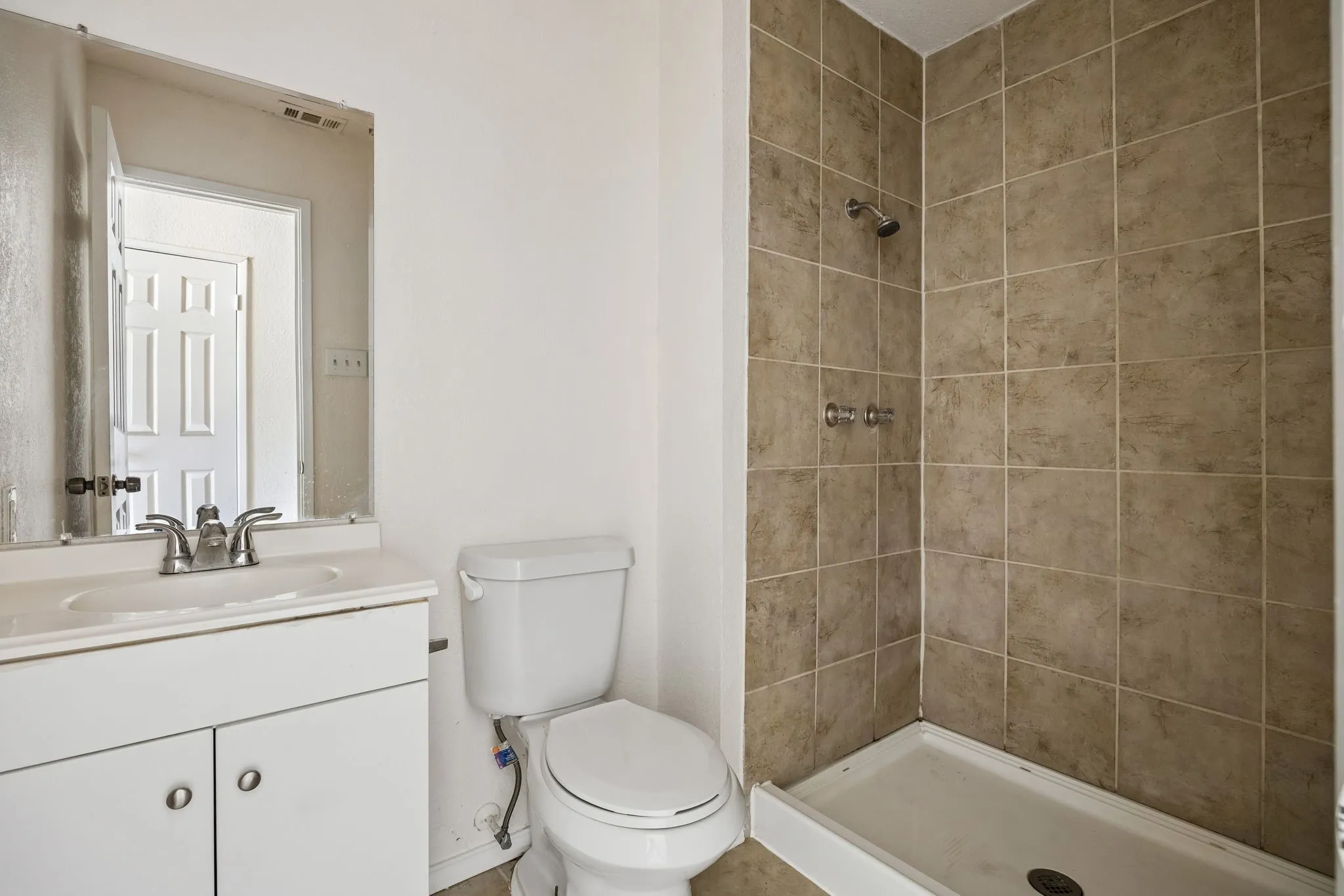 Bathroom featuring a vanity with an integrated sink, a commode, a walk-in shower with tile surround, and a wall-mounted mirror