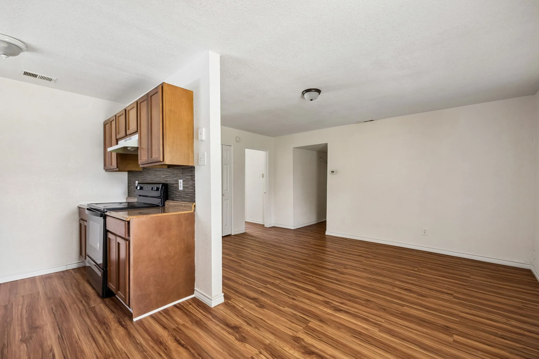 Kitchenette with wood-finish cabinetry, dark countertop, and a tiled backsplash