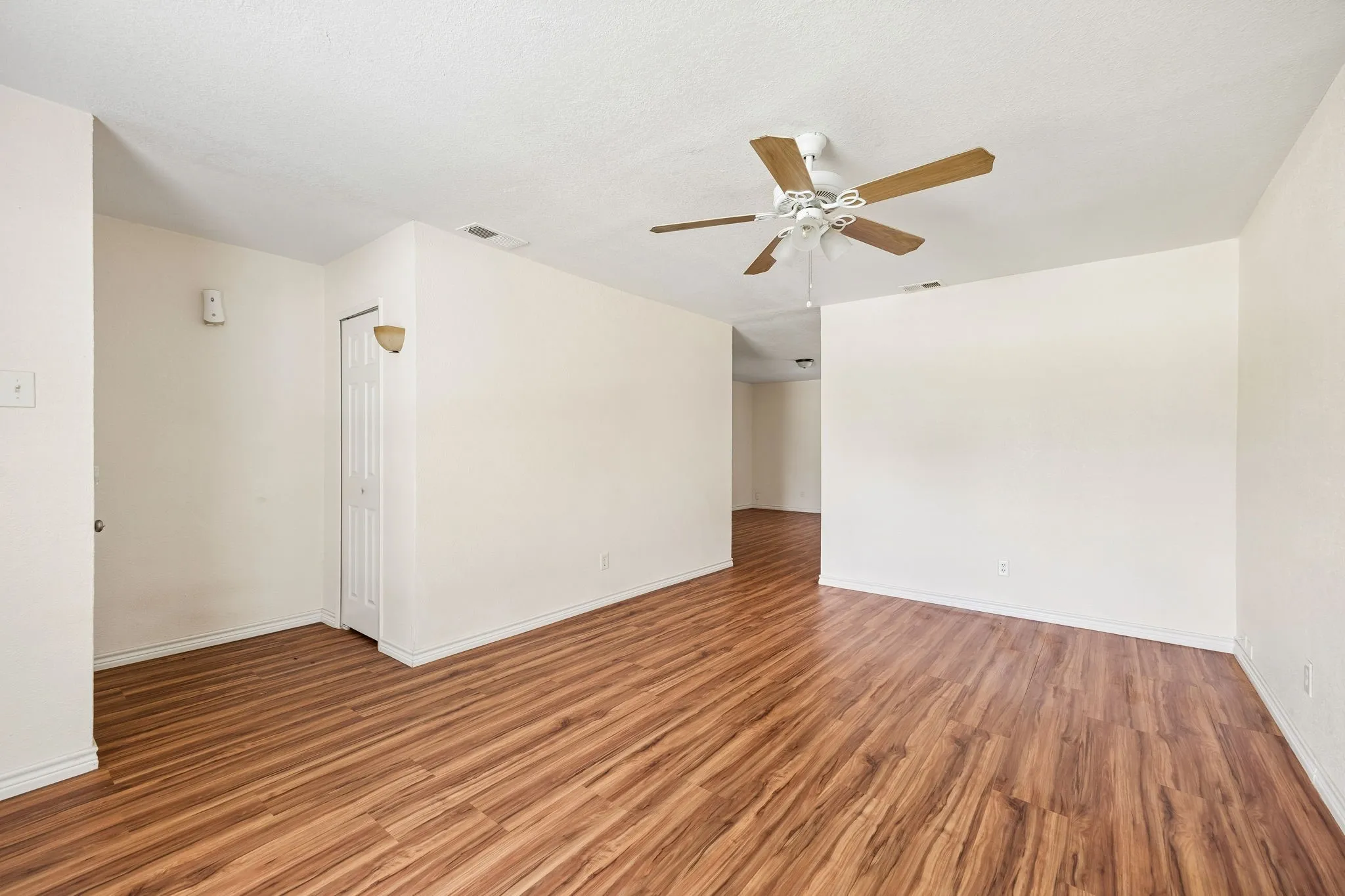 Open-concept living area featuring wood-finish flooring, a ceiling fan with wood-tone blades, and neutral wall tones