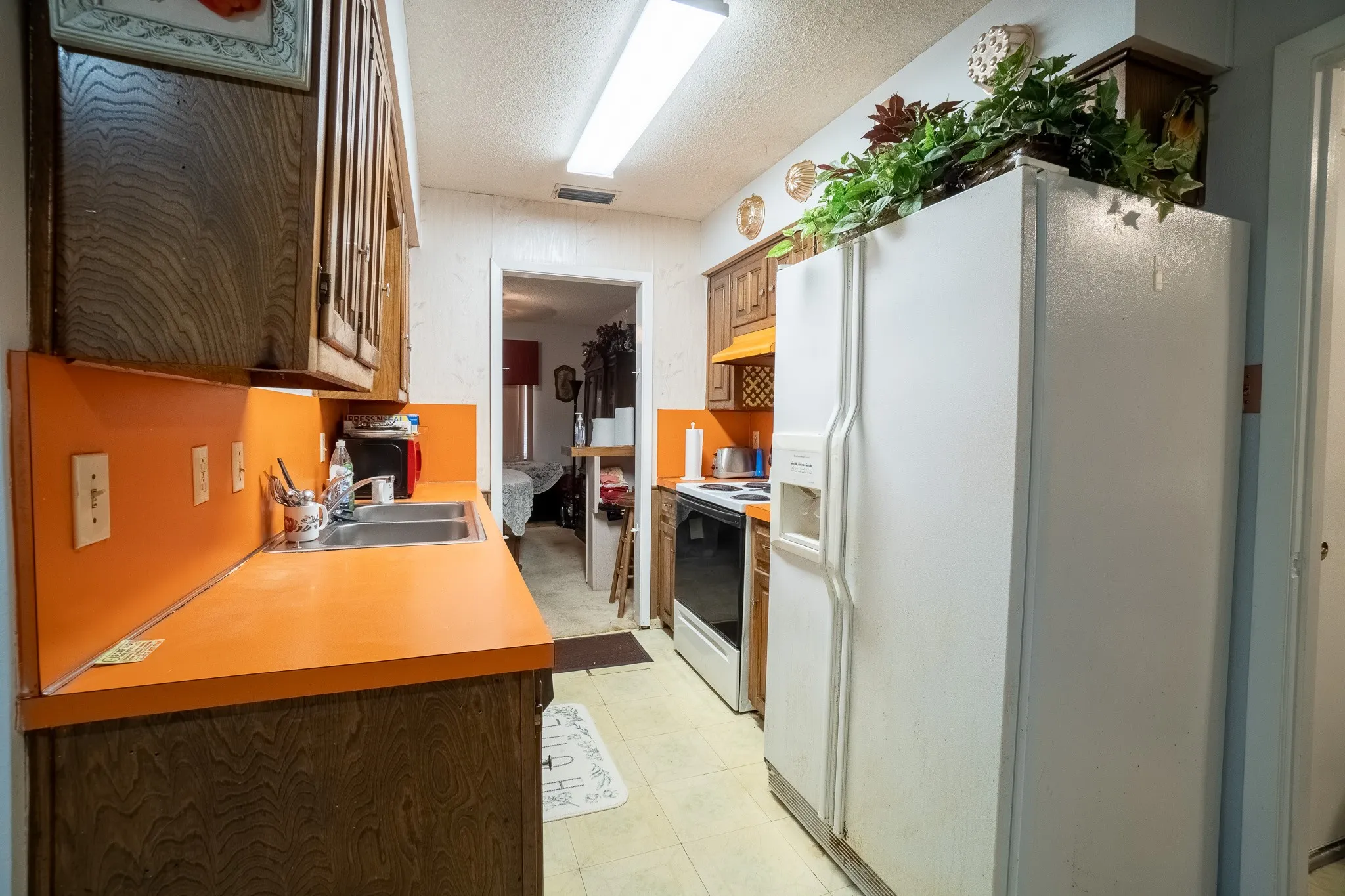 Kitchen featuring wood-finish cabinetry, orange laminate countertops, double basin stainless steel sink, white side-by-side refrigerator, and white electric range
