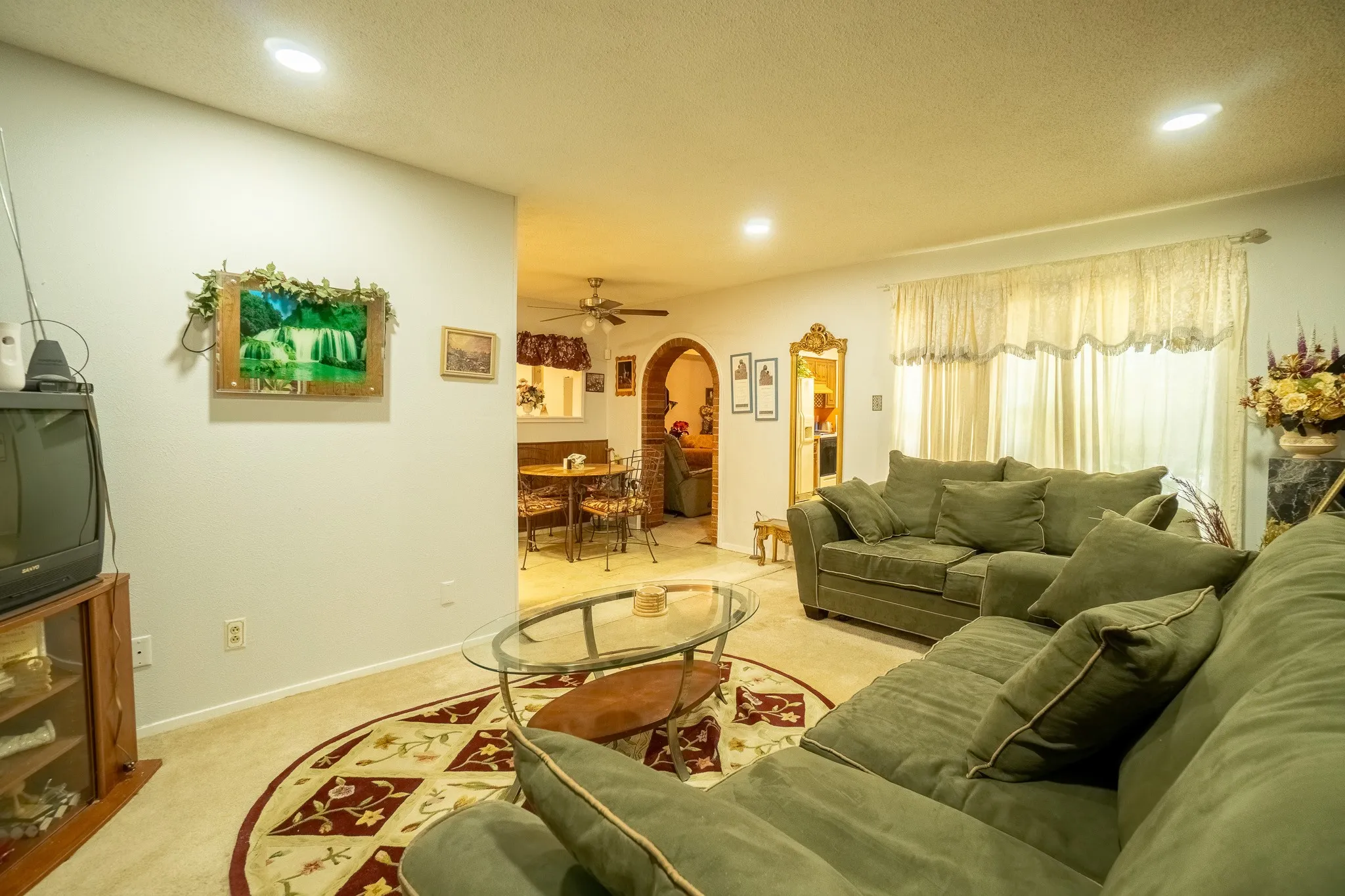 Carpeted living area featuring recessed lighting, a window with sheer curtains, and a rounded archway entry to an adjacent space