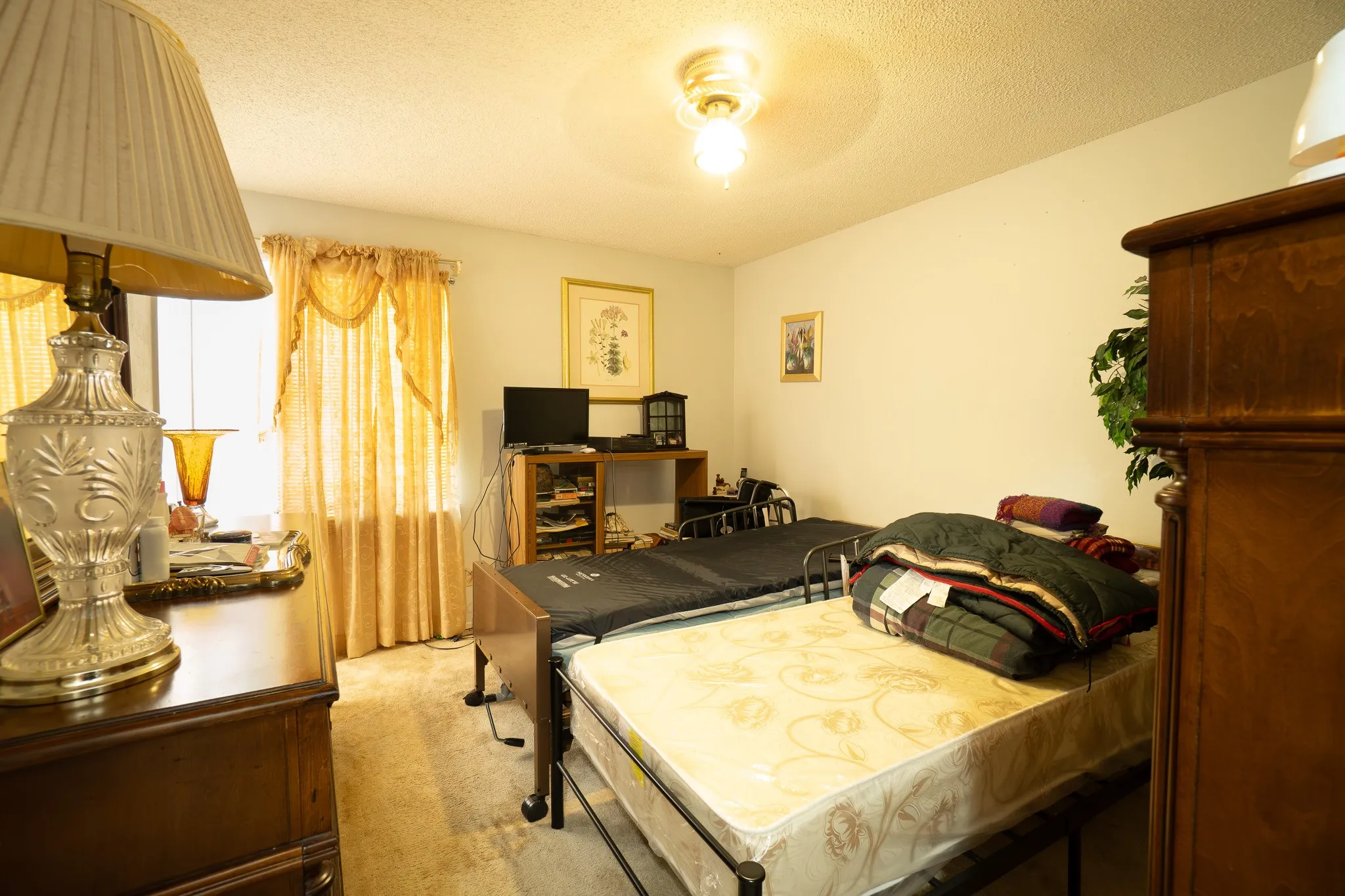 Carpeted room with a ceiling-mounted light fixture, light-colored walls, and a window featuring drapes
