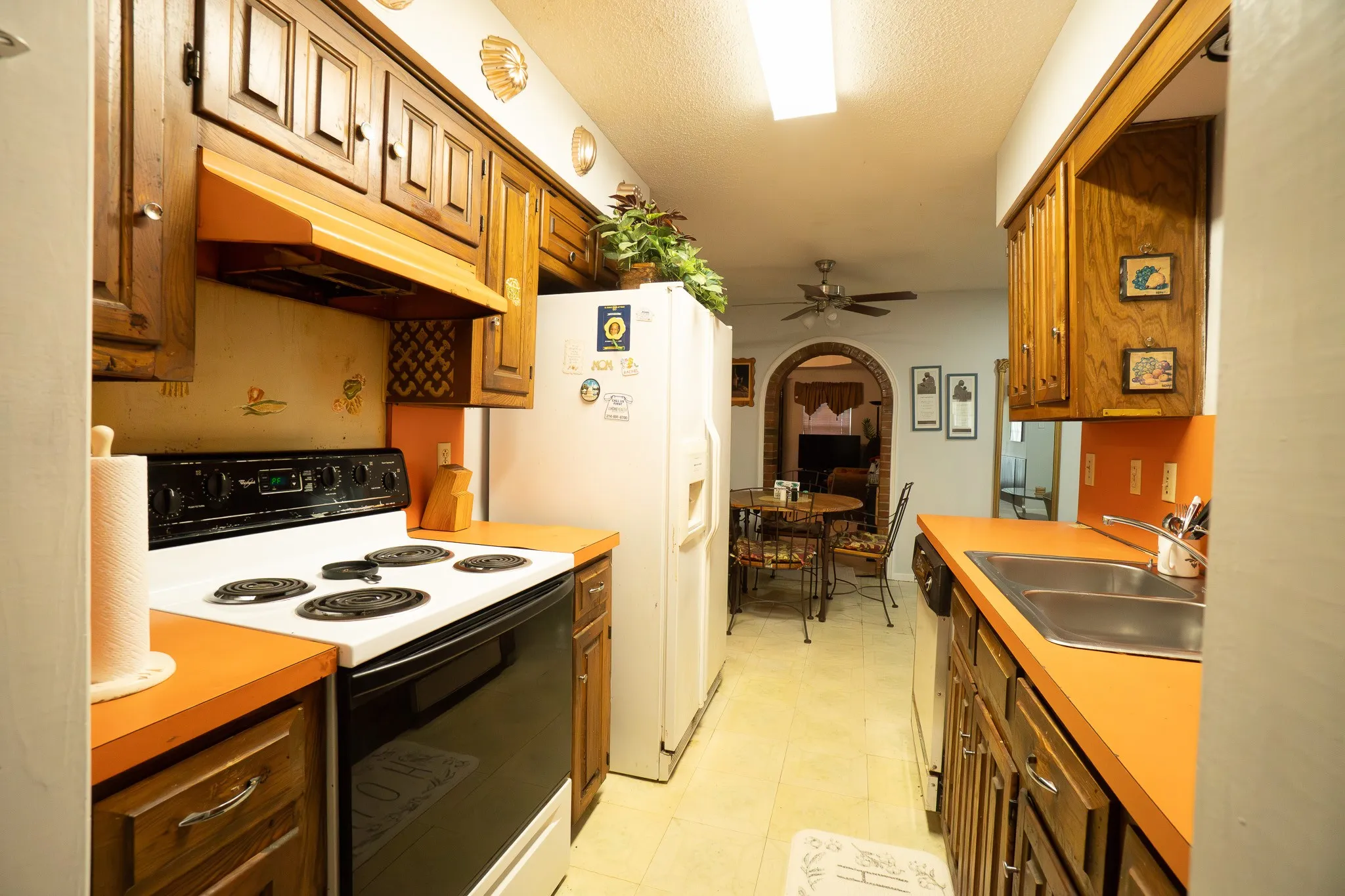 Galley kitchen featuring wood cabinetry, orange countertops, a white electric range, and a dual basin stainless steel sink