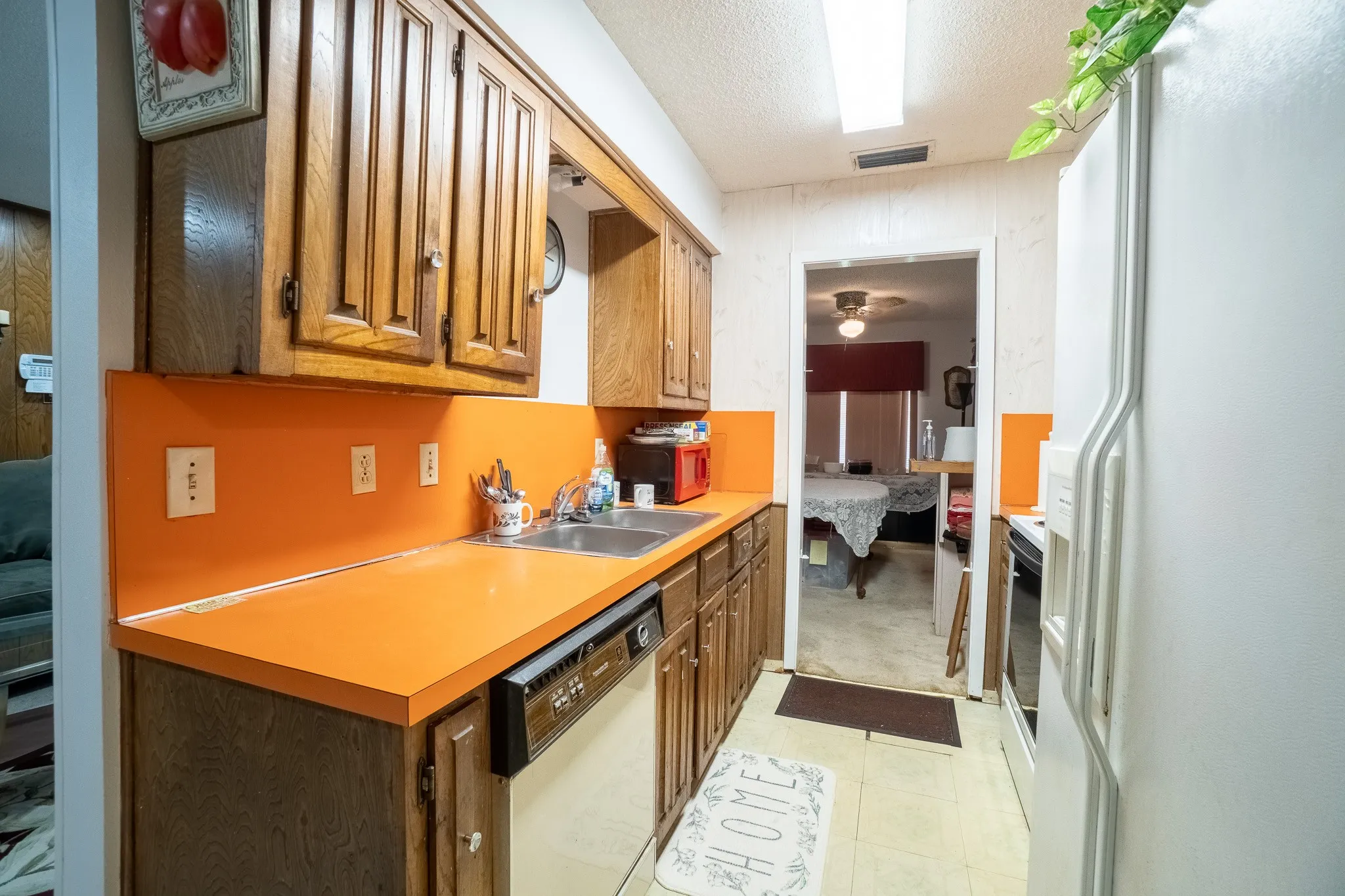 Galley kitchen featuring wood cabinetry, orange countertops, a stainless steel double sink, and a built-in dishwasher