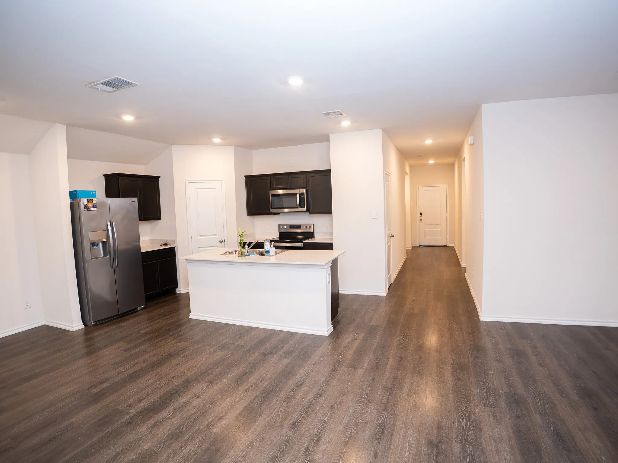 Open-concept living space featuring wood-finish flooring, a kitchen island with a built-in sink, dark cabinetry, stainless steel appliances, and recessed lighting