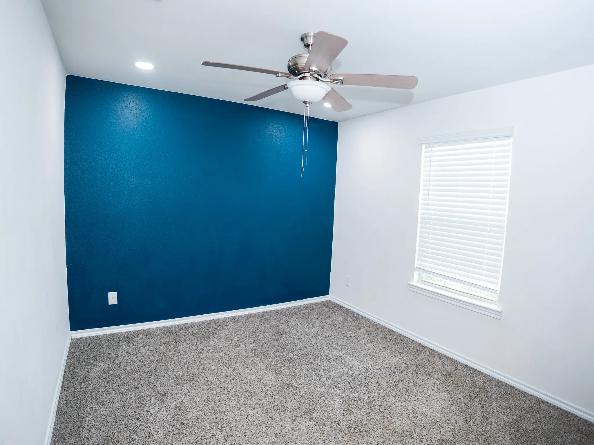 Interior room featuring a deep blue accent wall, neutral carpeting, and white baseboards