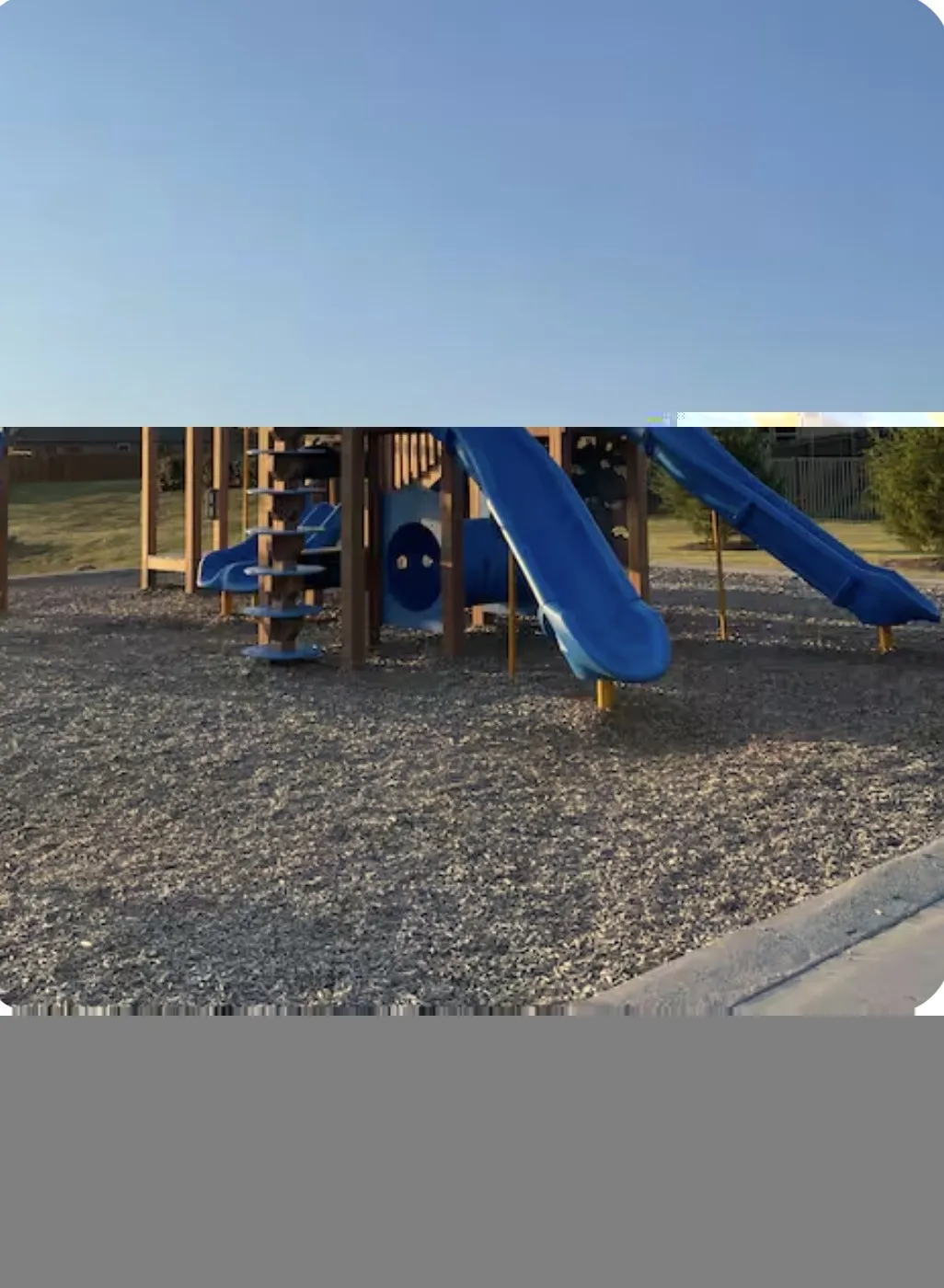 Outdoor play structure featuring multiple blue slides, a climbing wall, and a tunnel