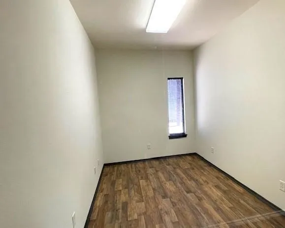 Room featuring wood-finish flooring, light-toned walls, and a rectangular window with blinds