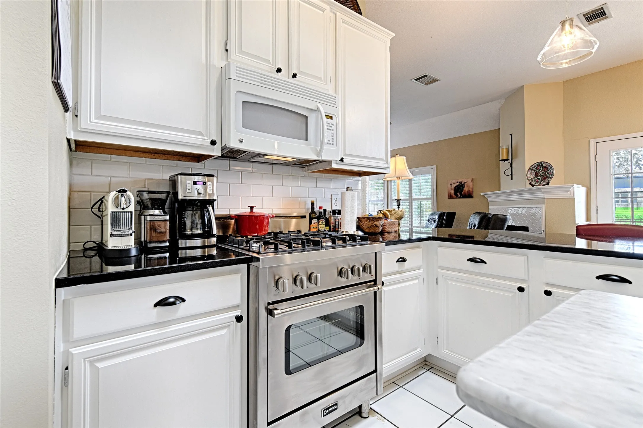 Well-appointed kitchen featuring white cabinetry, black countertops, stainless steel range with overhead microwave, and white subway tile backsplash