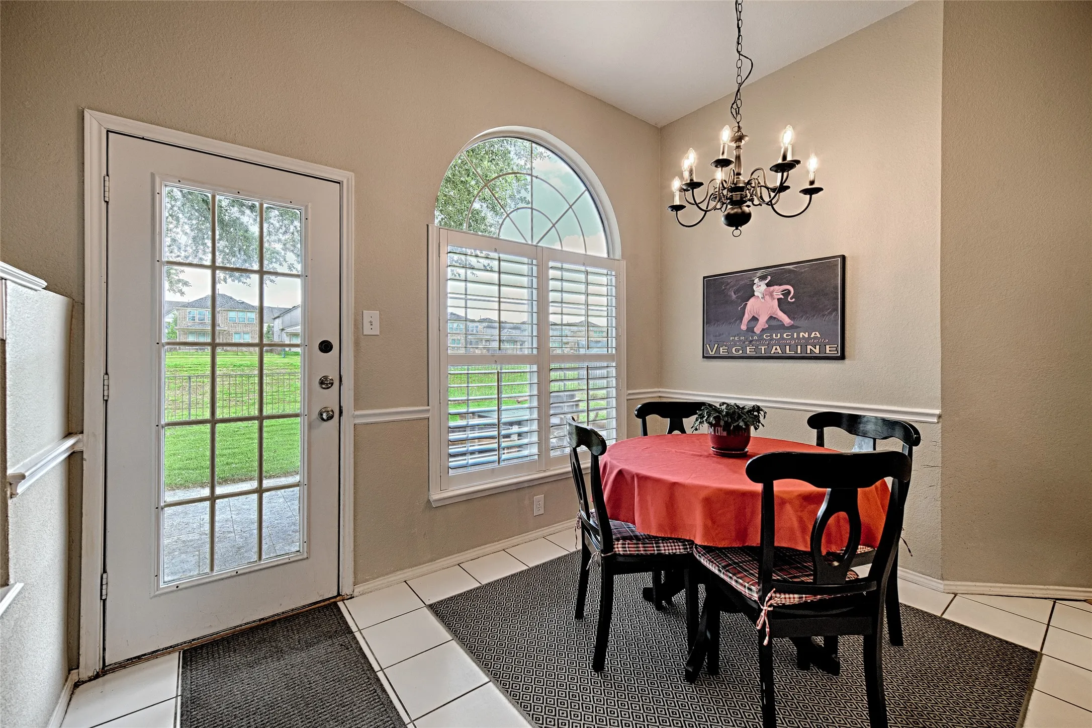 Dining area featuring a vaulted ceiling, a chandelier, and an arched window with louvered shutters