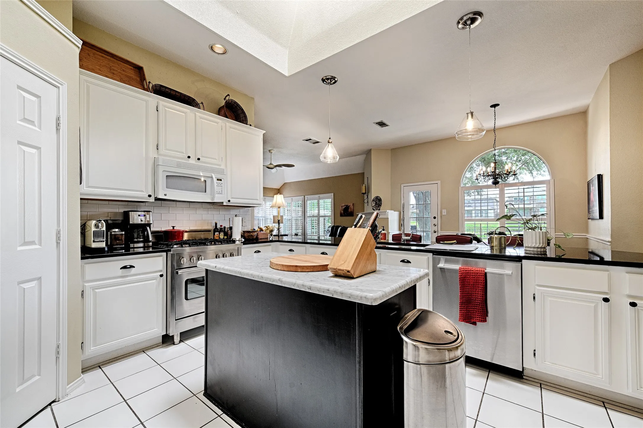 Kitchen featuring a central island with a light-toned countertop, white cabinetry with dark hardware, black countertops, stainless steel appliances, and white tile flooring