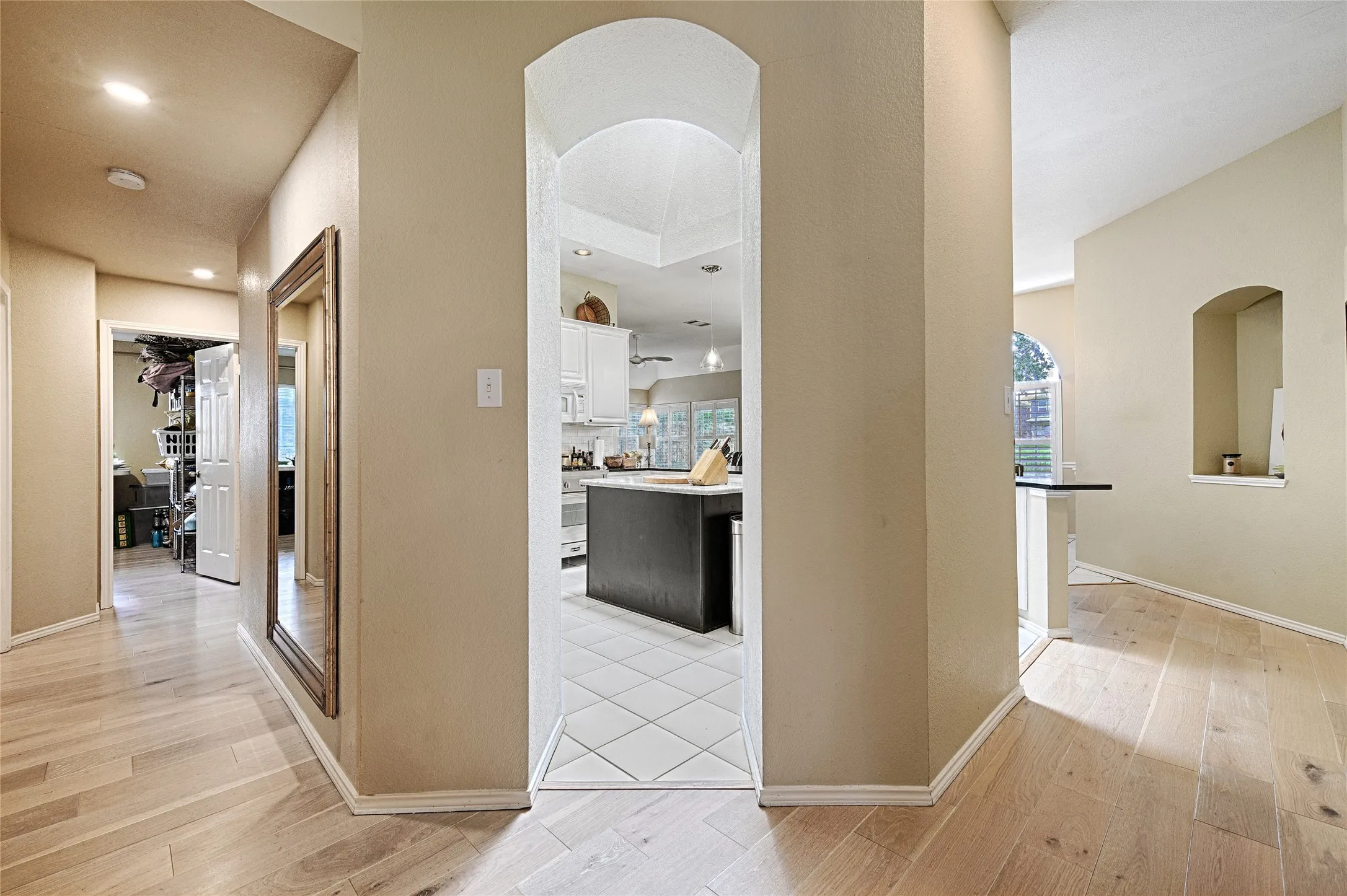 Archway entrance with tile flooring leading into a kitchen featuring white cabinetry and a dark central island