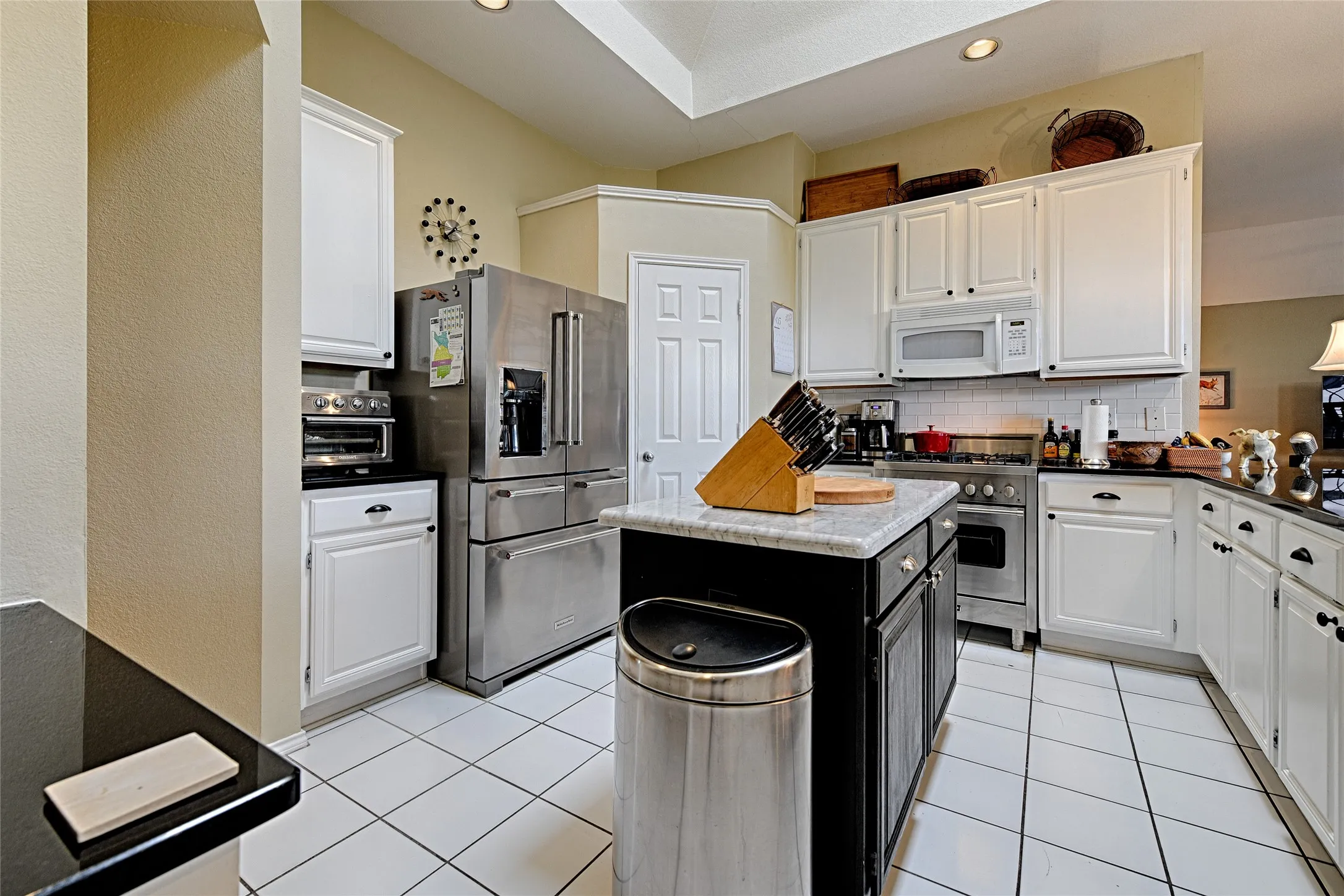 Kitchen featuring white cabinetry, black countertops, a central island with a light-toned countertop, a stainless steel refrigerator, and a stainless steel range oven