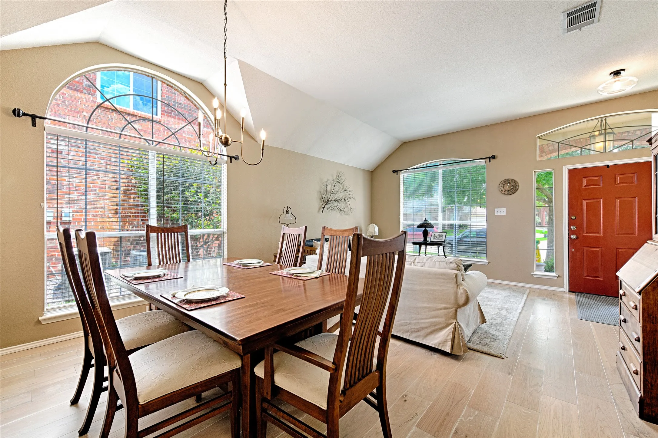 Vaulted ceiling space featuring wood-finish flooring, a prominent arched window with transom detail, and a vibrant red entry door with sidelights
