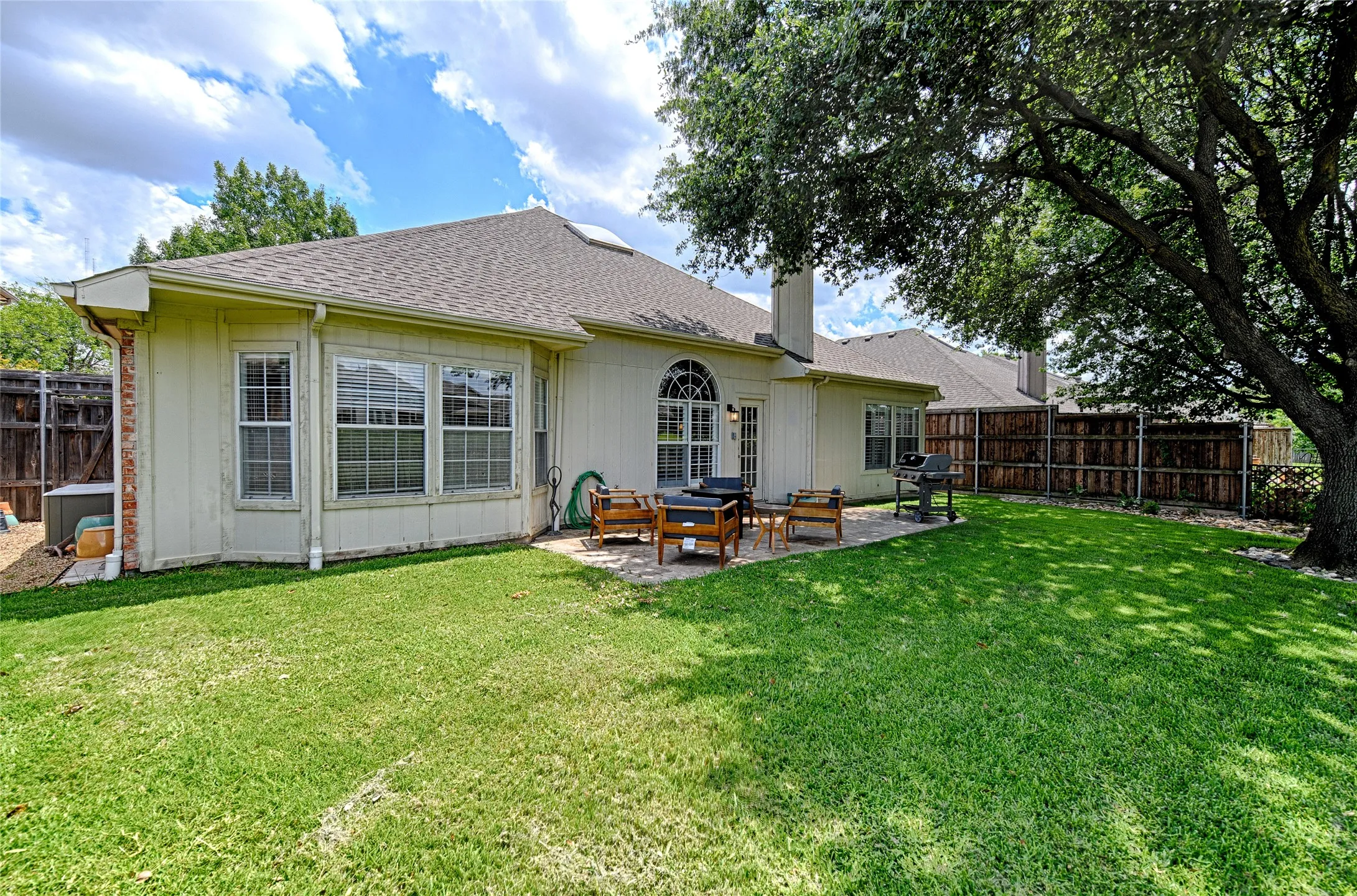 Spacious backyard featuring a large grass lawn, mature shade tree, and a stone patio
