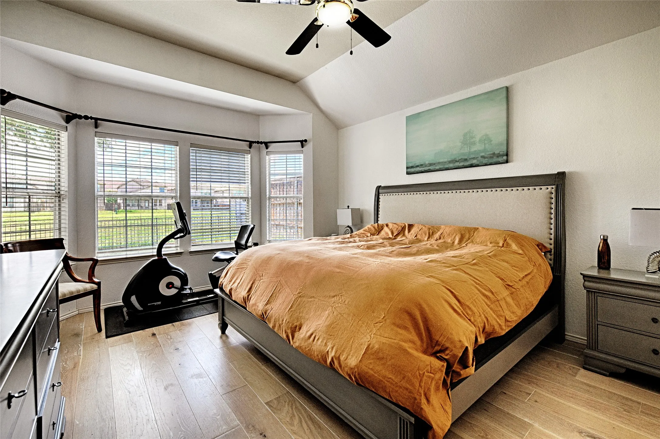 Vaulted ceiling bedroom featuring wood-finish flooring, a bay window with blinds, and a ceiling fan