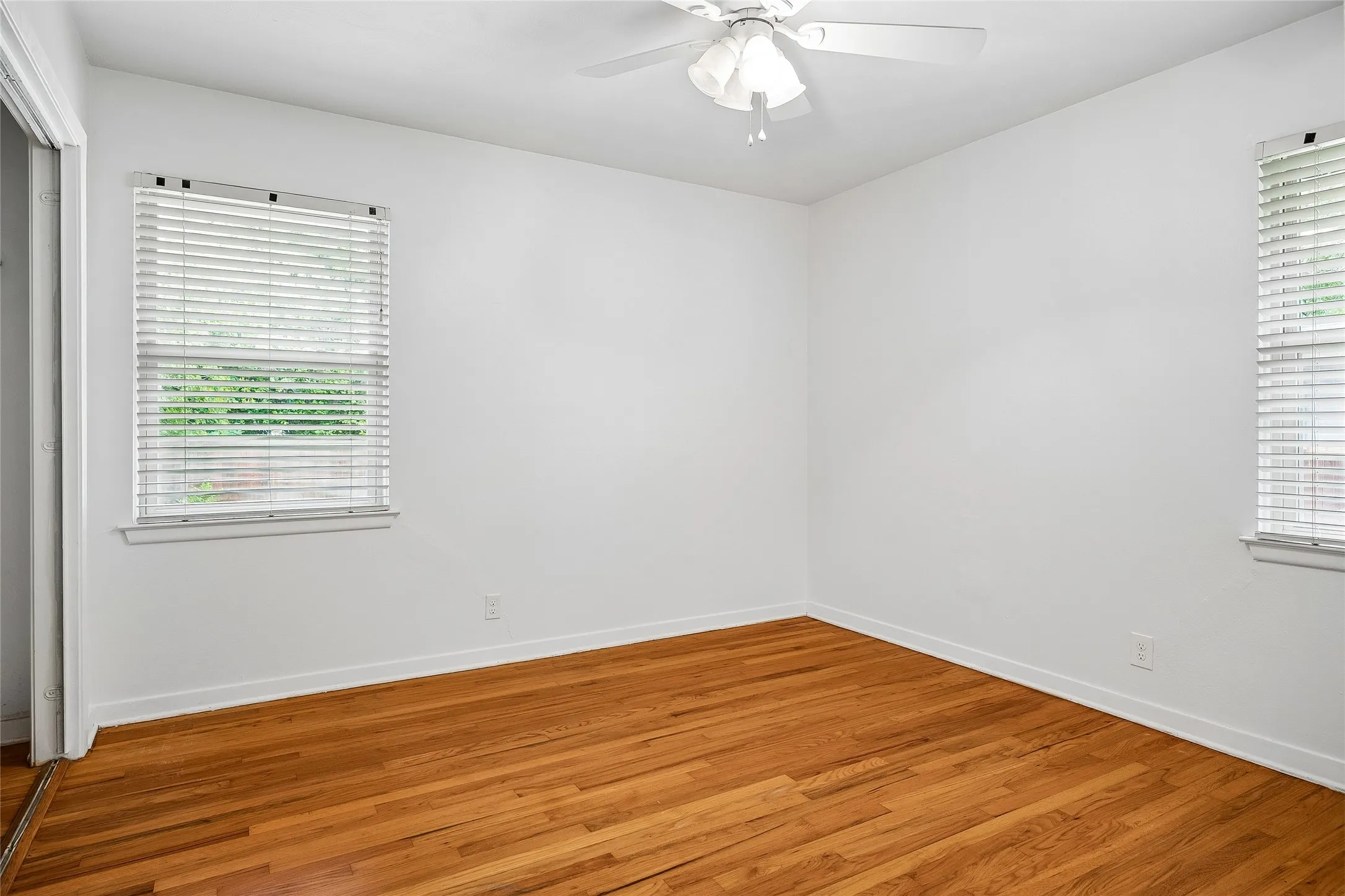 Hardwood flooring, white wall paneling, ceiling fan with light fixture, window with blinds, and white trim