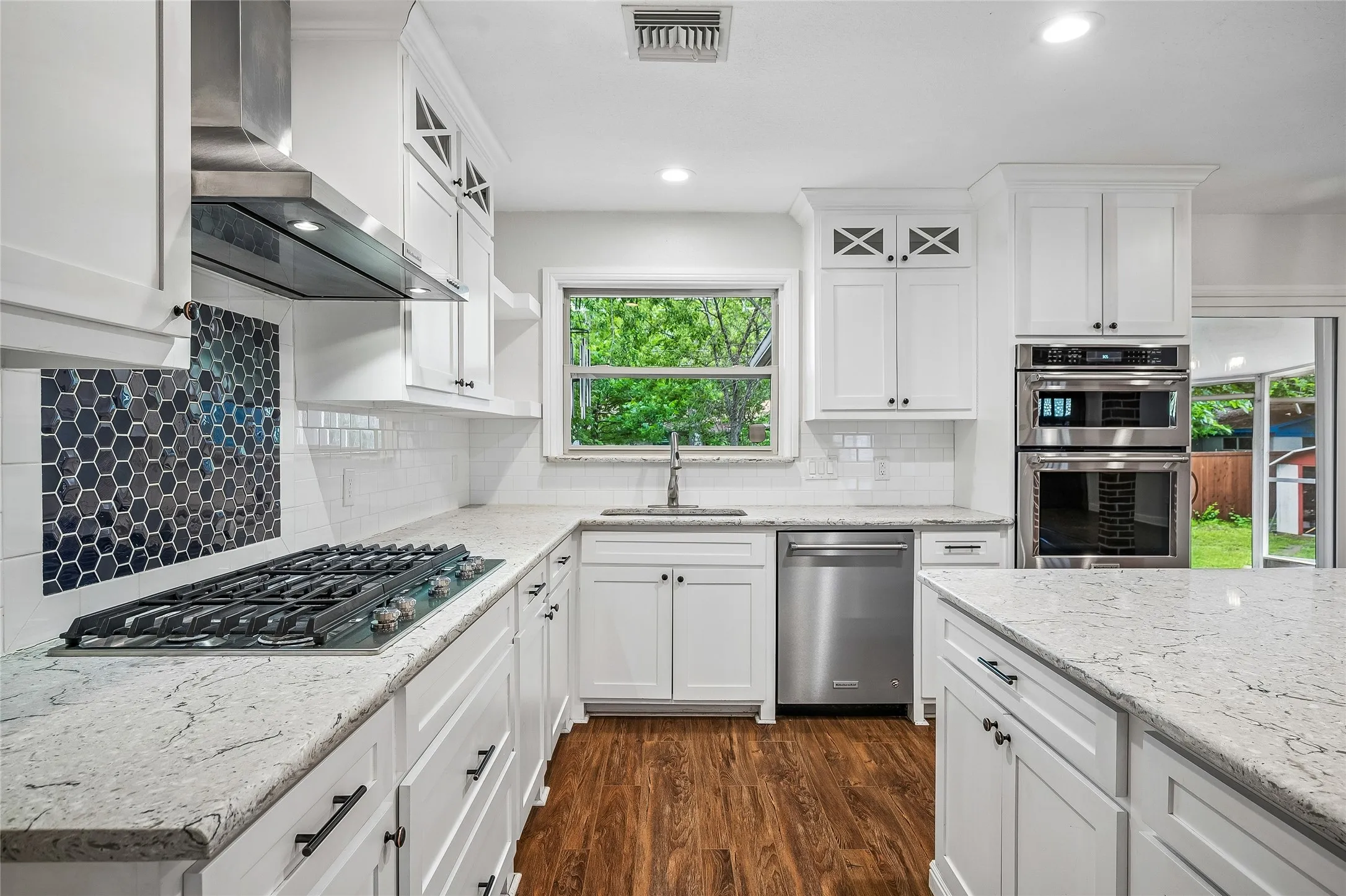 Open-concept kitchen featuring an island with a light-toned countertop, white cabinetry with dark hardware, built-in stainless steel appliances, and wood-finish flooring