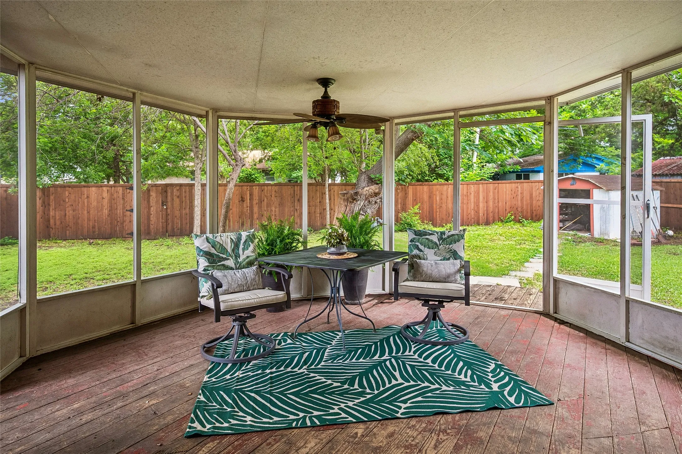 Screened outdoor living area featuring wood-finish flooring, a ceiling fan, and direct access to the backyard