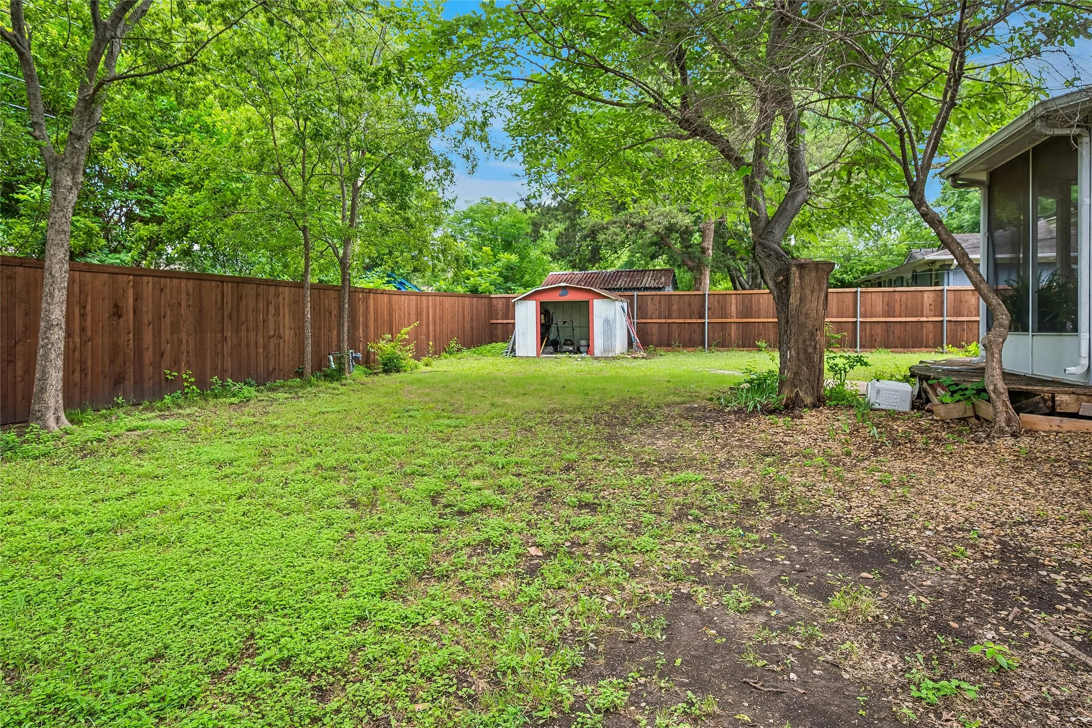 Expansive rear yard featuring a privacy fence, established trees, a storage shed, and a screened porch area
