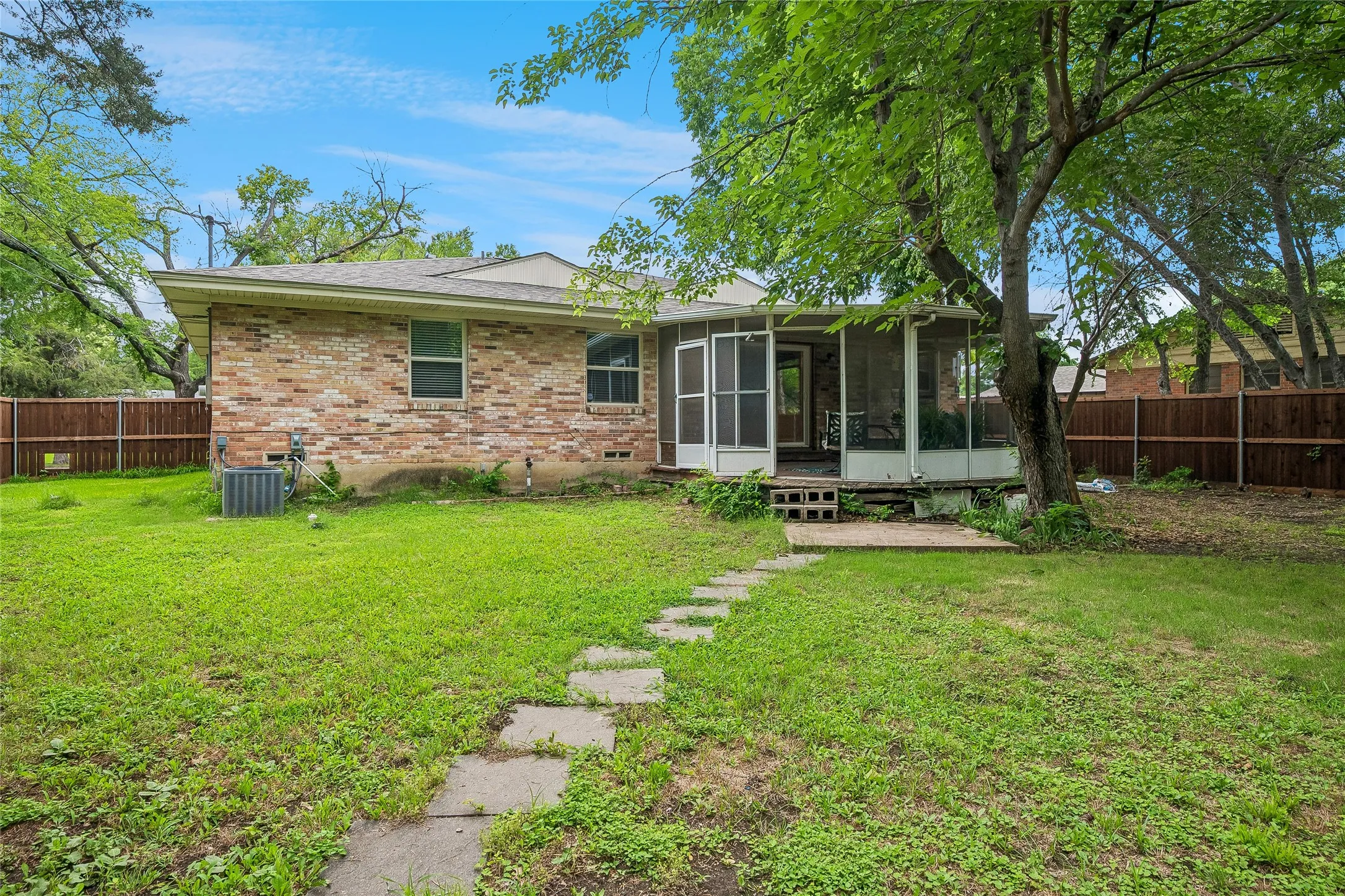 Expansive backyard featuring a screened porch, mature tree coverage, brick exterior, and a privacy fence