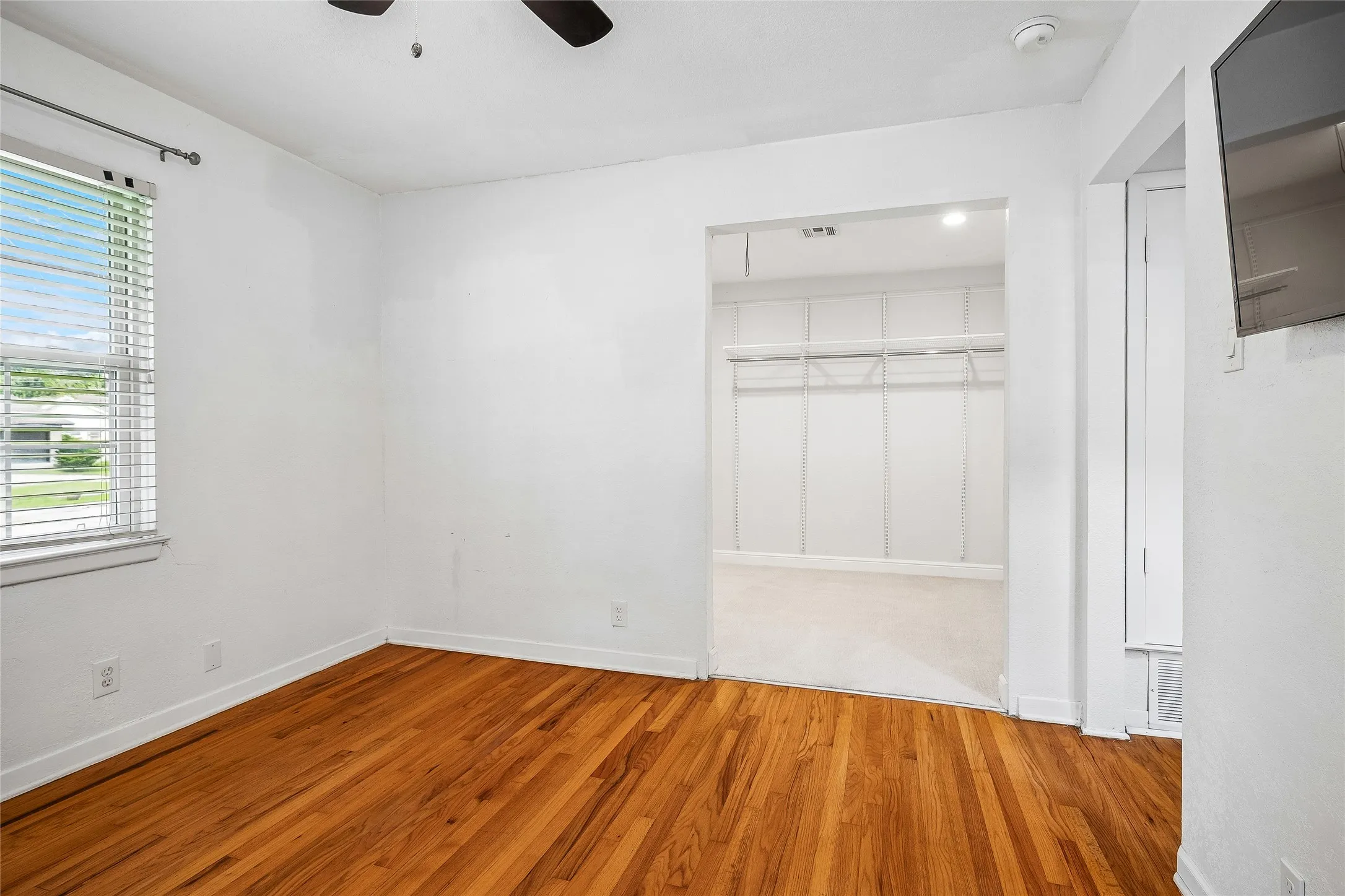 Room featuring wood flooring, neutral wall tones, two windows with blinds, and a ceiling fan with integrated lighting