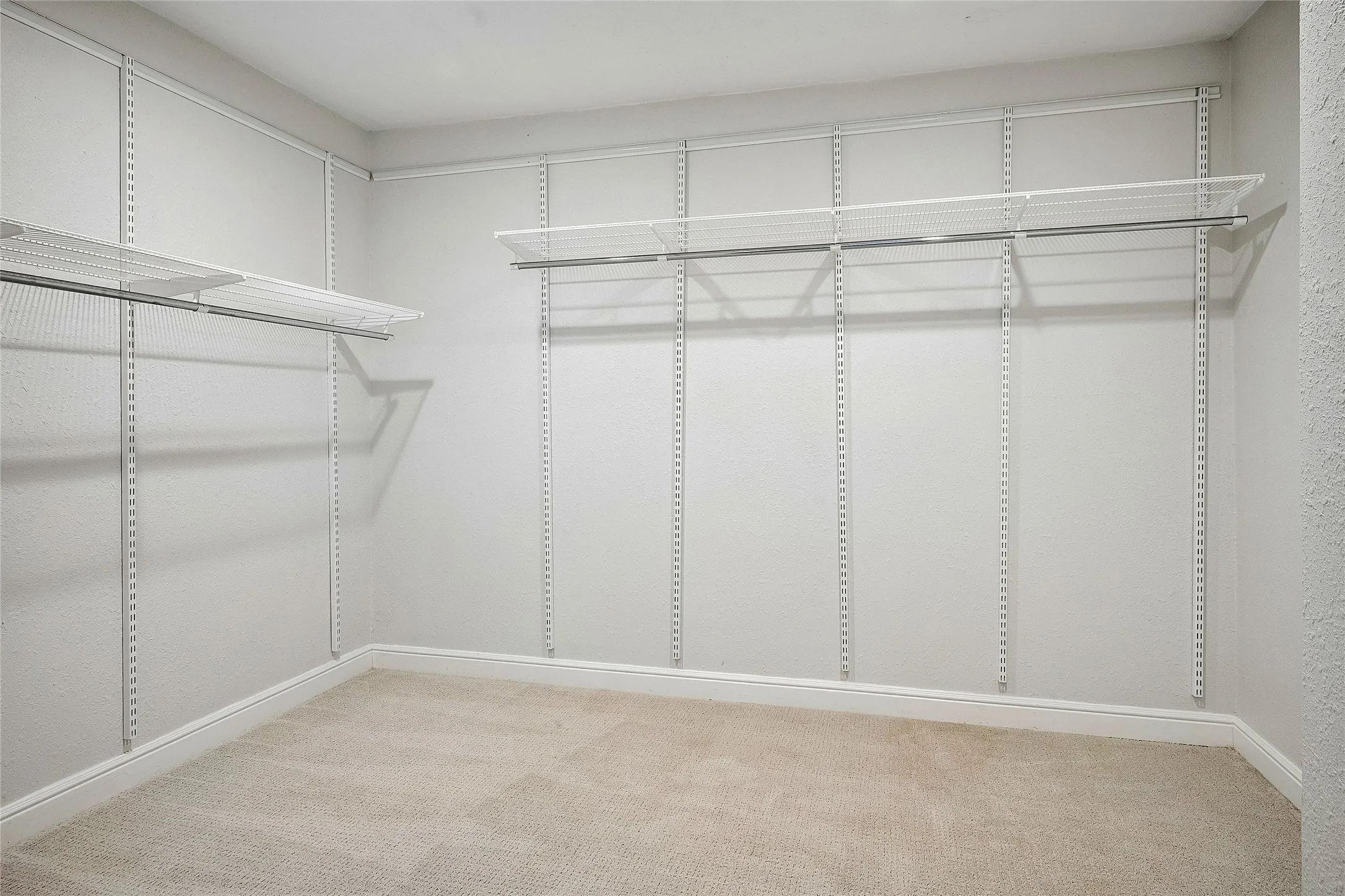 Main bedroom closet, 8x10 Walk-in  featuring adjustable wire shelving, integrated hanging rods, plush carpet flooring, and white baseboard trim