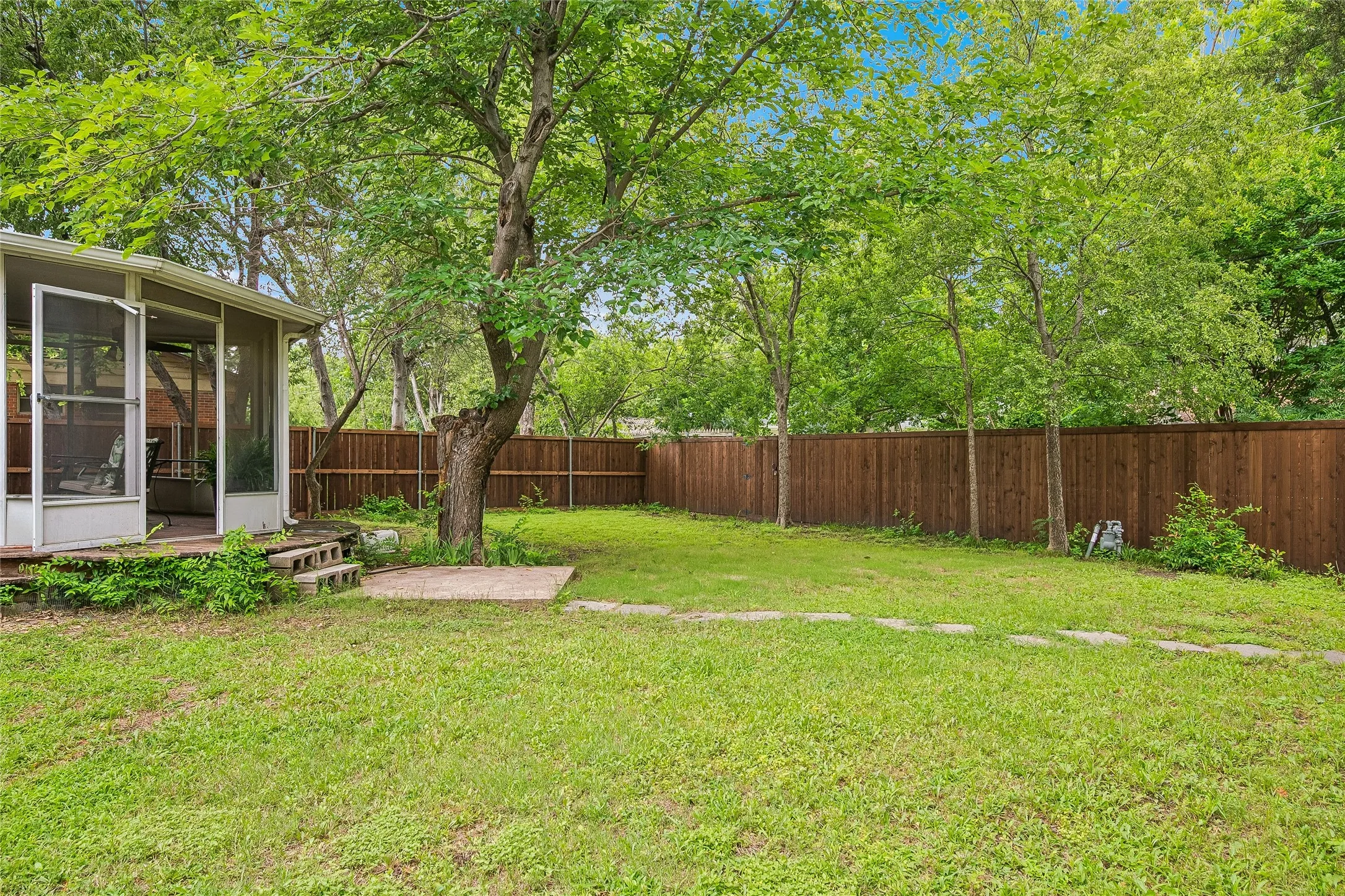 Expansive lawn area featuring a large mature tree, wood privacy fencing, and an enclosed screened porch with multiple entry points