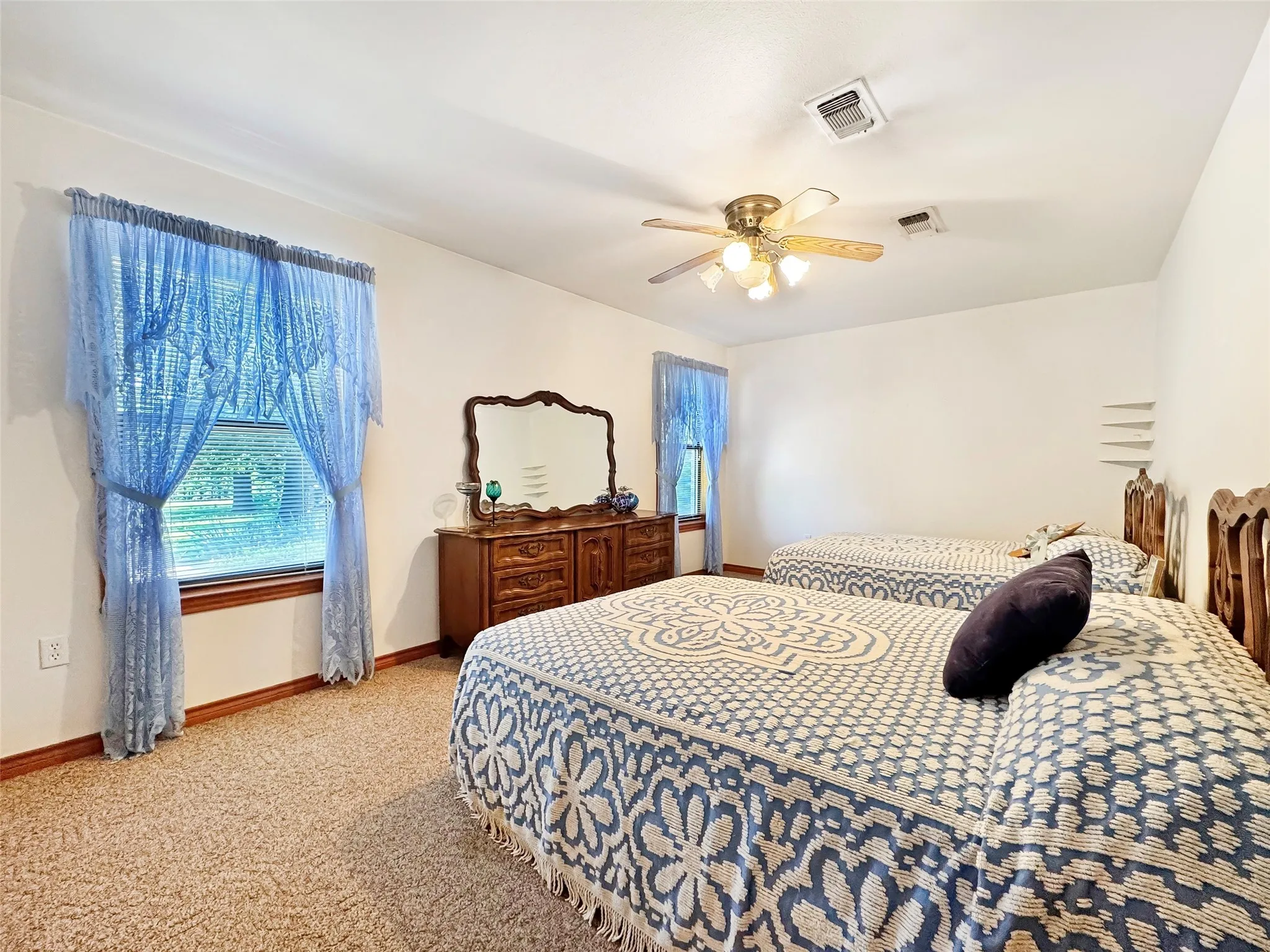 Carpeted interior space featuring a window with blue sheer curtains and a wood-finish baseboard