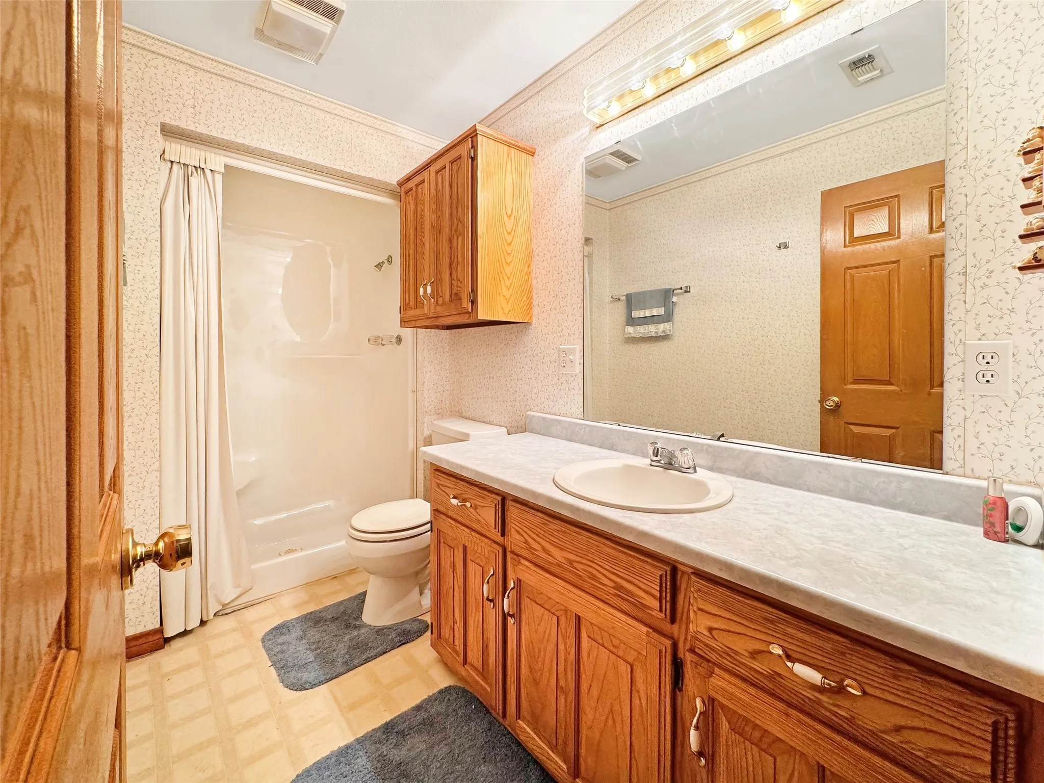 Bathroom featuring a single vanity with an integrated sink, a large wall-mounted mirror, and a shower with a privacy curtain