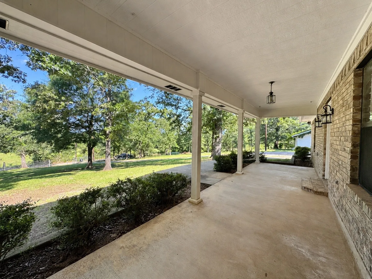 Expansive covered porch featuring a concrete surface, white columns, and brick exterior