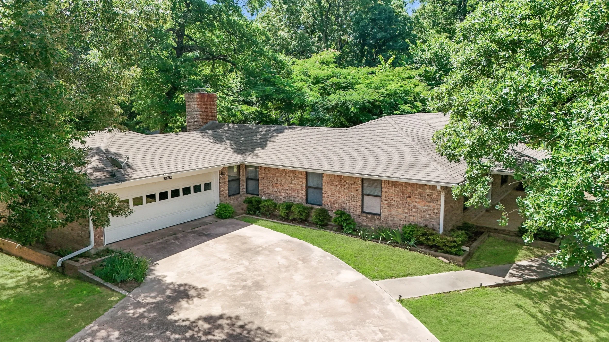 Brick exterior home featuring a two-car garage, concrete driveway, and mature landscaping