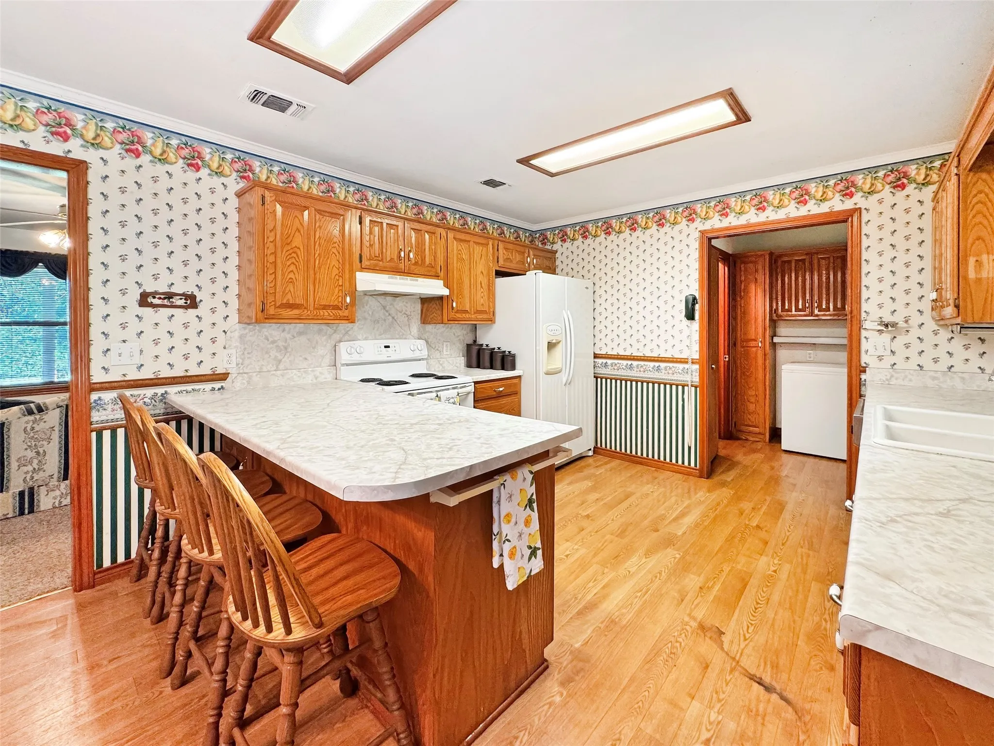Kitchen featuring wood-finish flooring, wood cabinetry, white appliances, a breakfast bar, and recessed lighting