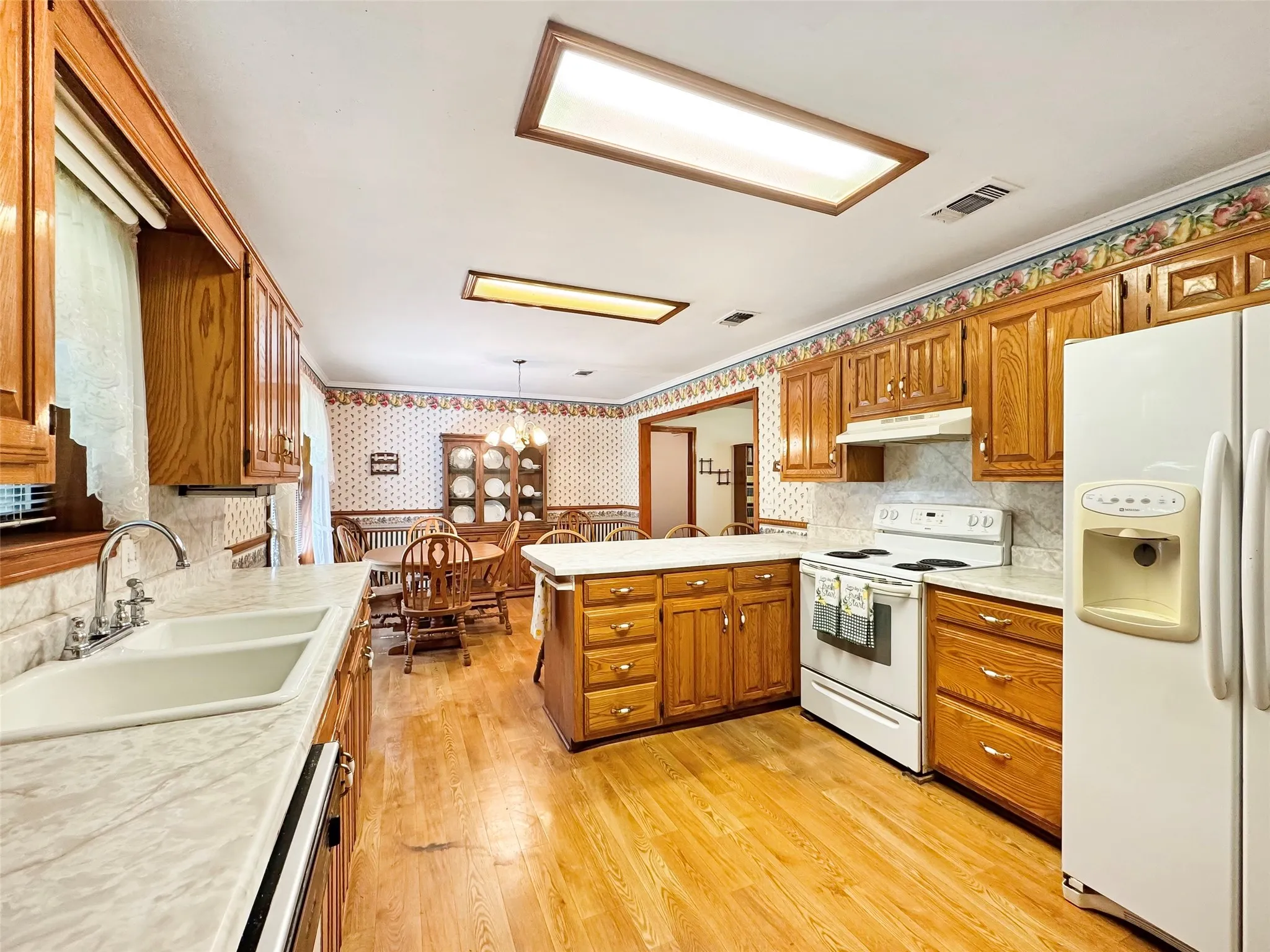 Kitchen featuring wood-finish cabinetry, white appliances, and a central island with countertop