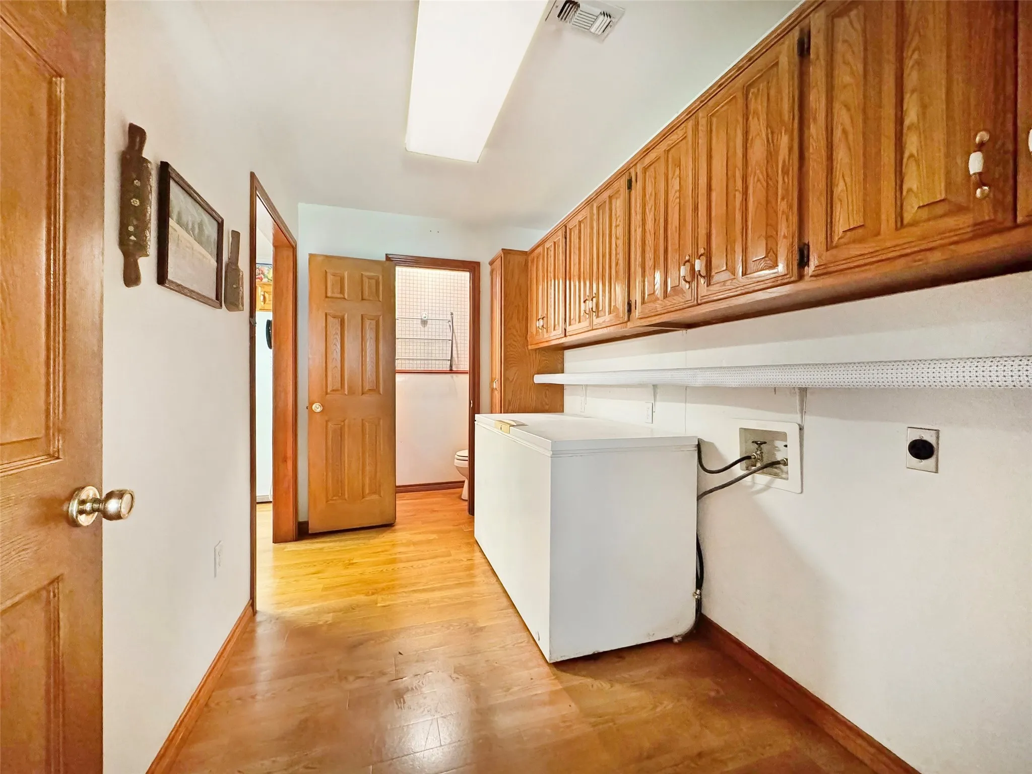 Utility area featuring wood-finish flooring, shaker-style upper cabinetry, and a white wall-mounted shelf