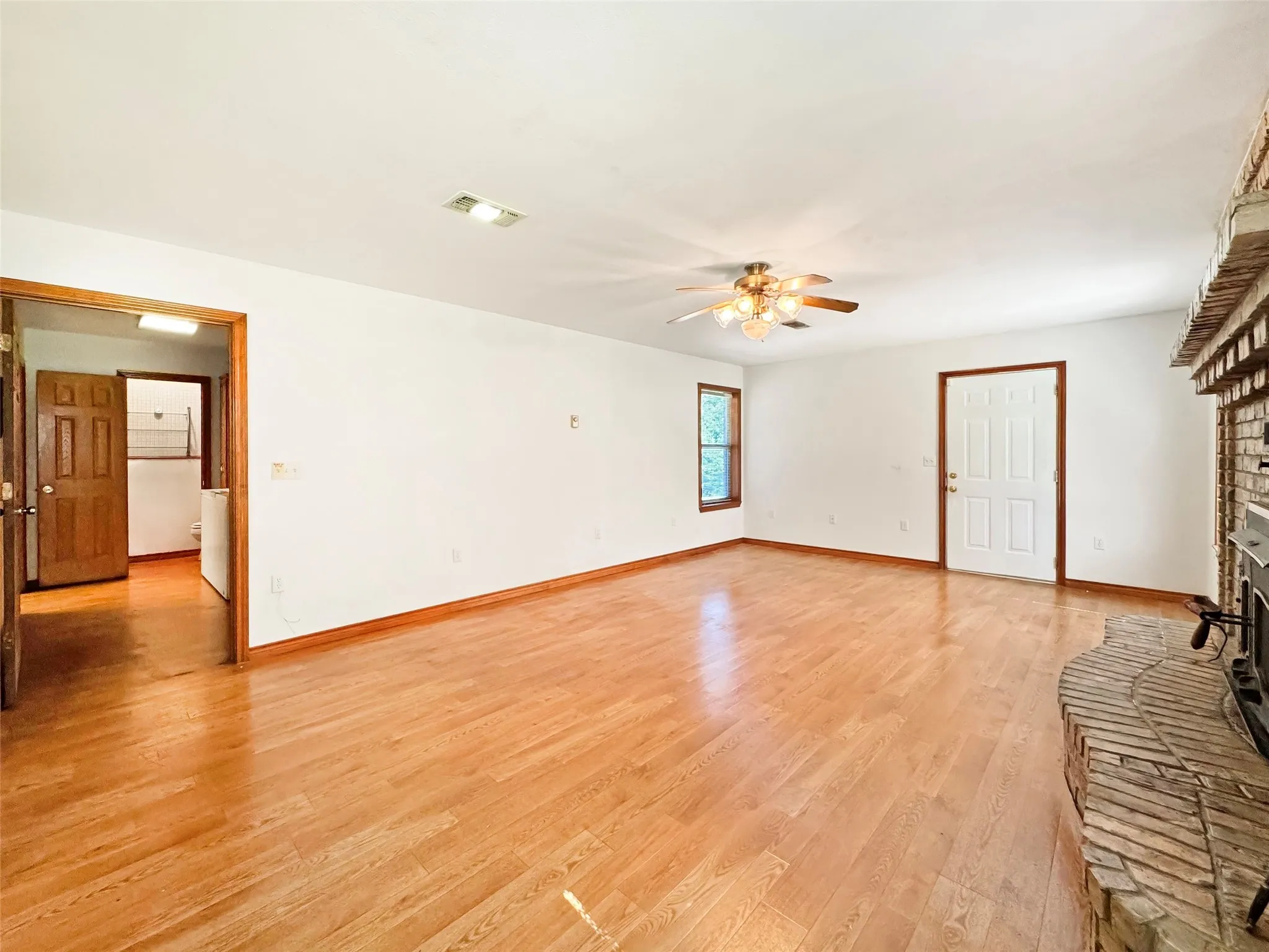 Spacious room featuring wood-finish flooring, a brick fireplace with a raised hearth, and a ceiling fan with integrated lighting