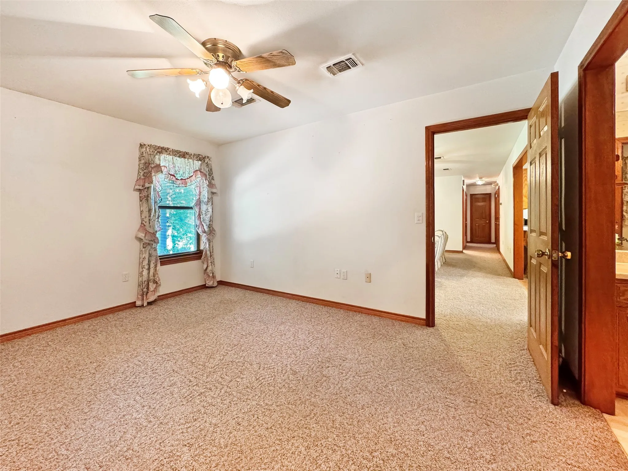 Carpeted room featuring a ceiling fan with light fixture, a single window, white walls, and wood-finish trim