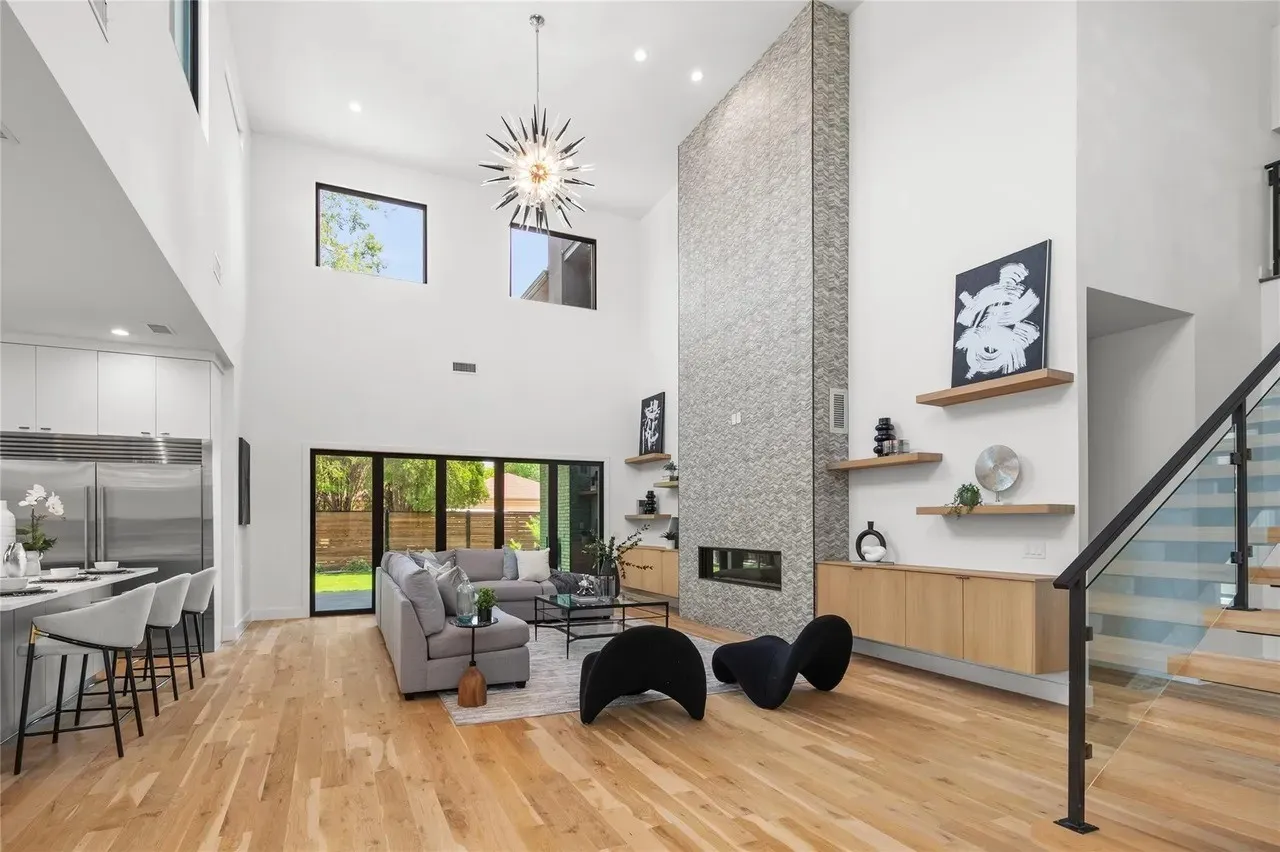 Expansive double-height living area featuring a floor-to-ceiling stone-clad fireplace and light wood-finish flooring