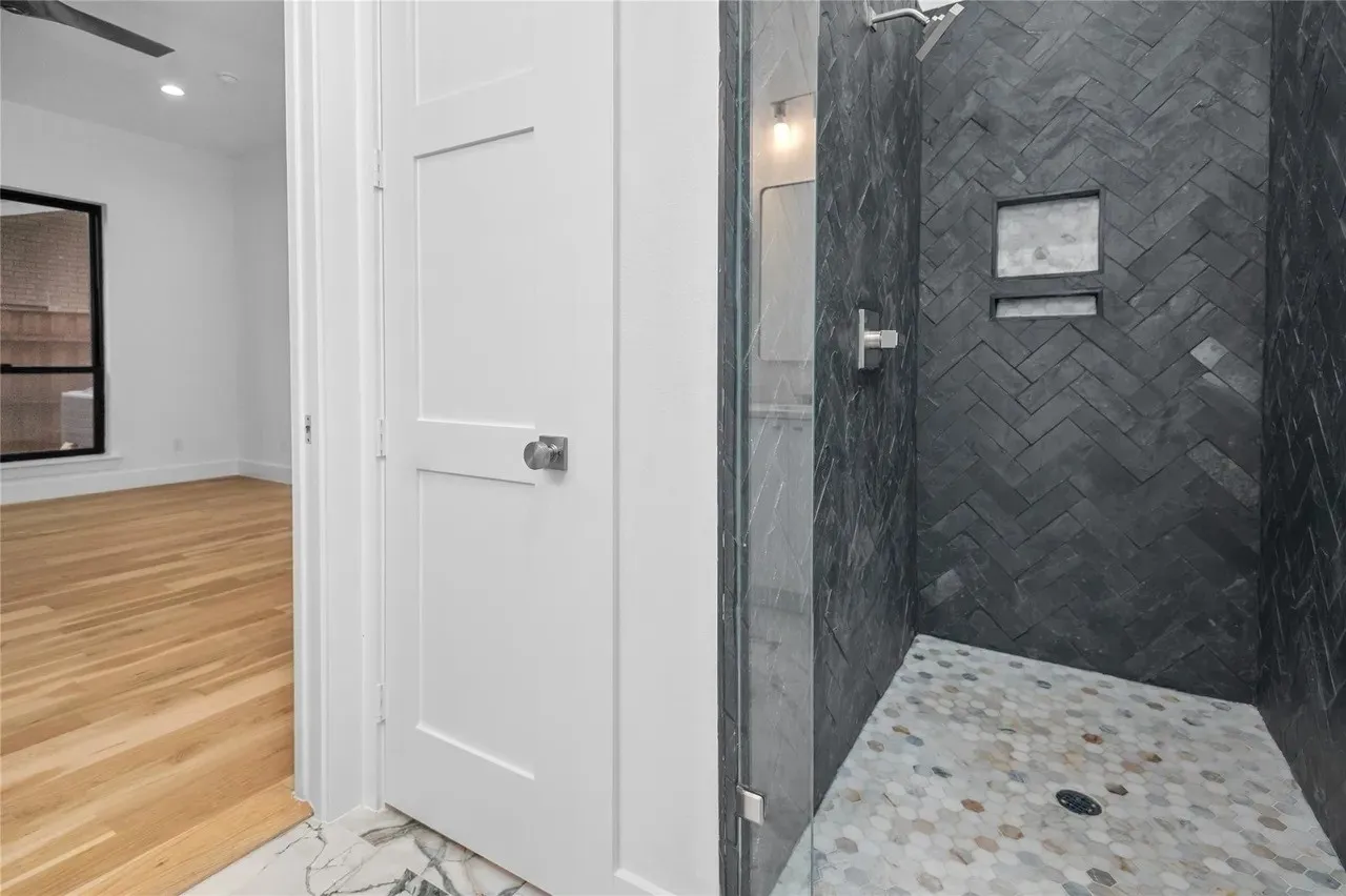 Walk-in shower featuring dark herringbone tile walls, an integrated niche, and a hexagonal tile floor